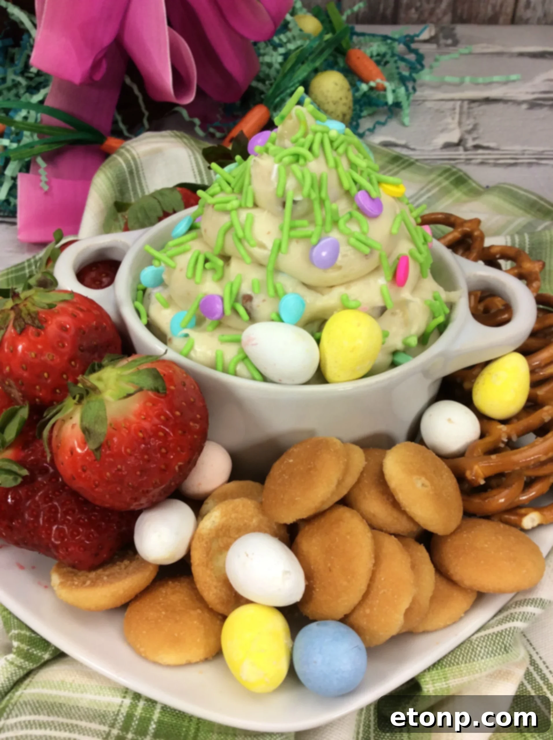 A beautifully piped Springtime Cheesecake Dip in a decorative white serving bowl, topped with whole and crushed Cadbury Mini Eggs, ready for a spring gathering.