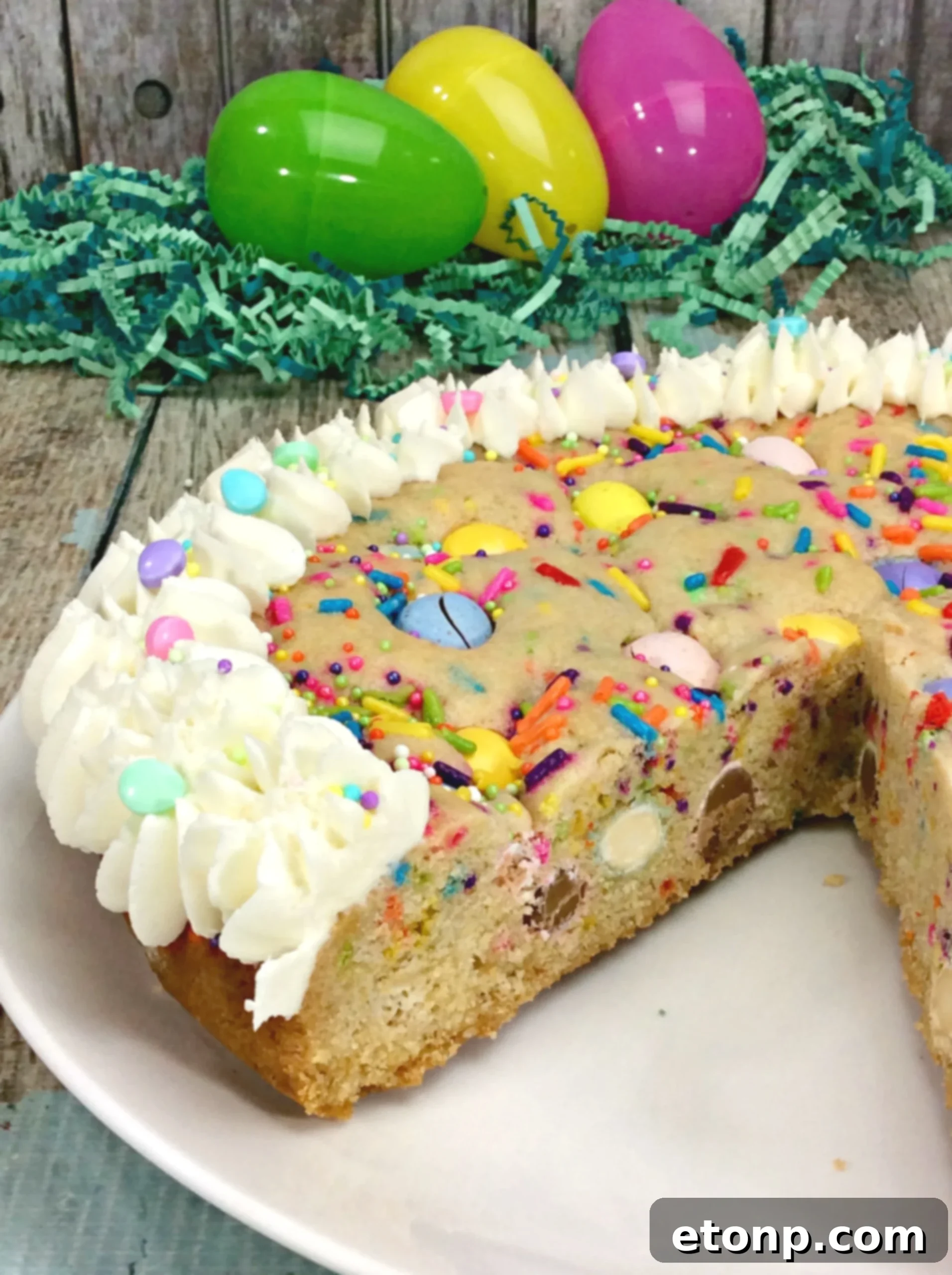 A perfectly sliced piece of Easter Cookie Pie on a white plate, showcasing the fluffy vanilla frosting piped around the edges and festive sprinkles.