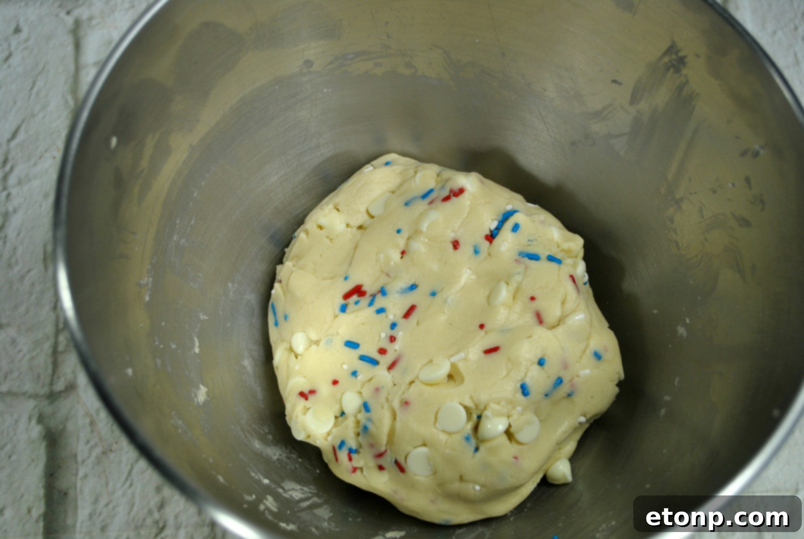 Dough balls of White Chocolate Firework Cookies rolled in sprinkles, ready for baking on a parchment-lined sheet.