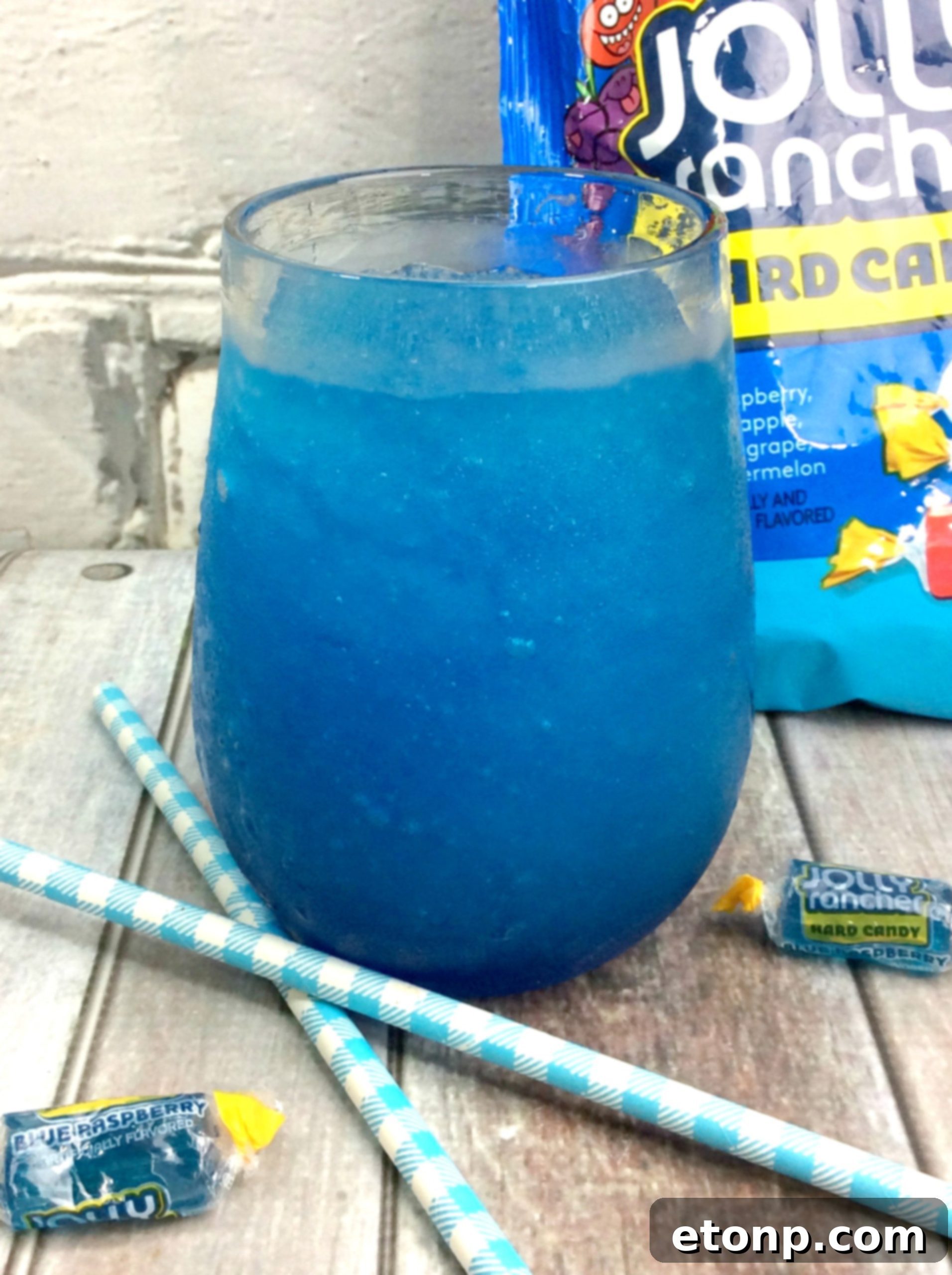 Blue Raspberry Jolly Rancher Slushy Cocktail in a glass with a straw, garnished with candy.
