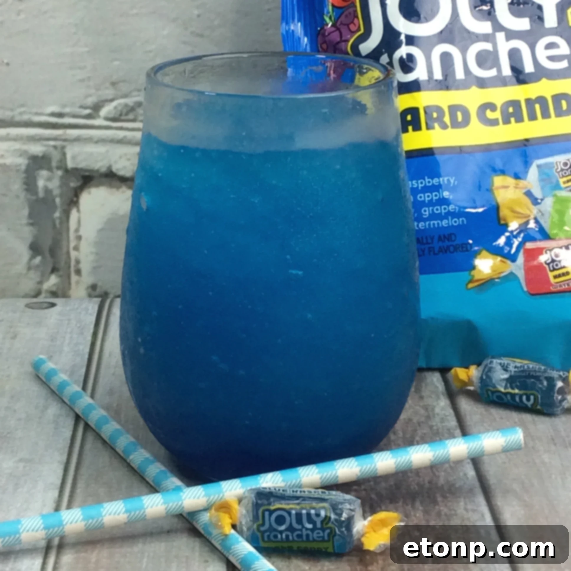 A glass of Blue Raspberry Jolly Rancher Cocktail garnished with a blue Jolly Rancher candy.
