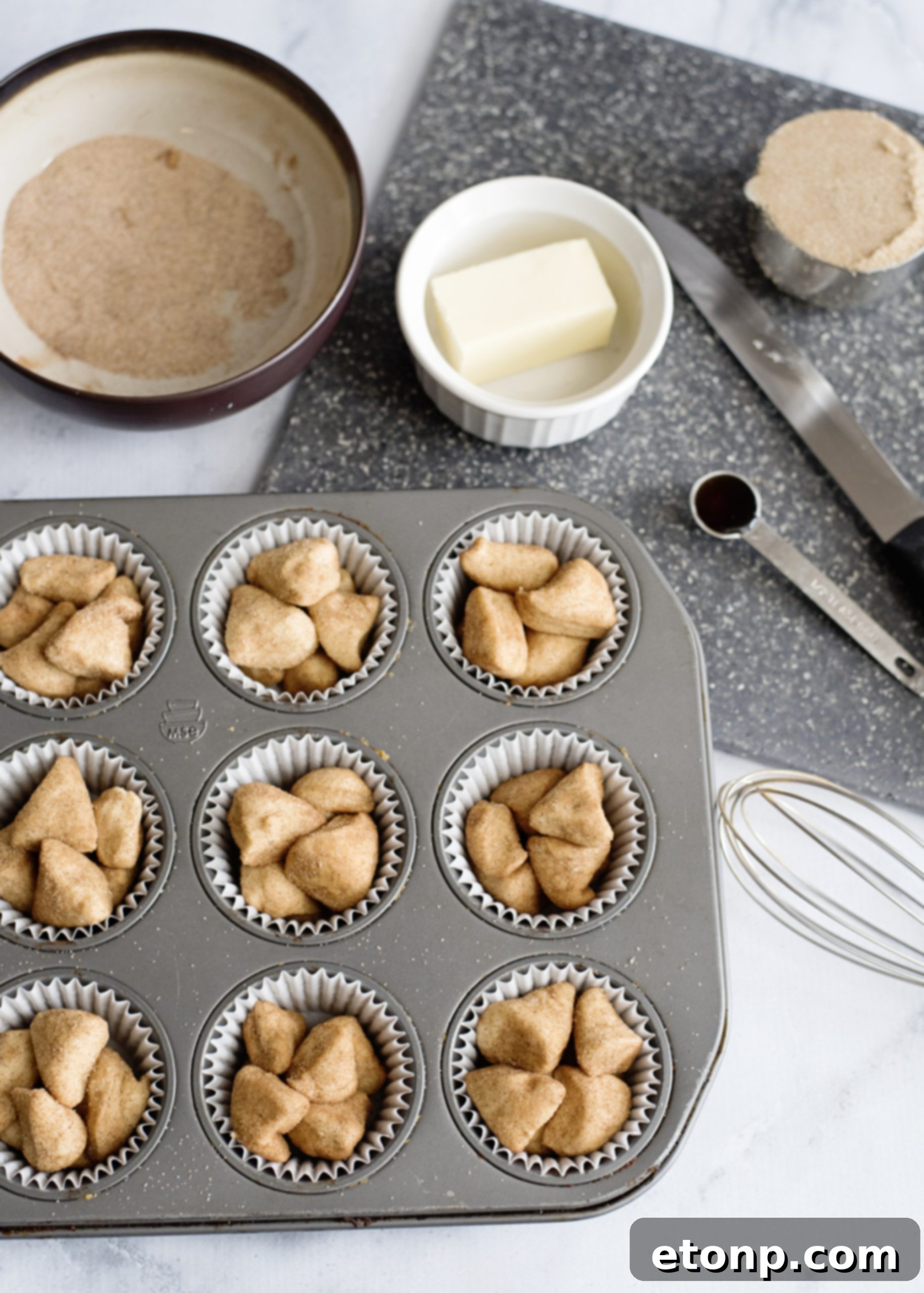 Raw biscuit dough pieces coated in cinnamon sugar, ready to be placed into muffin tins for Snickerdoodle Monkey Bread Muffins.