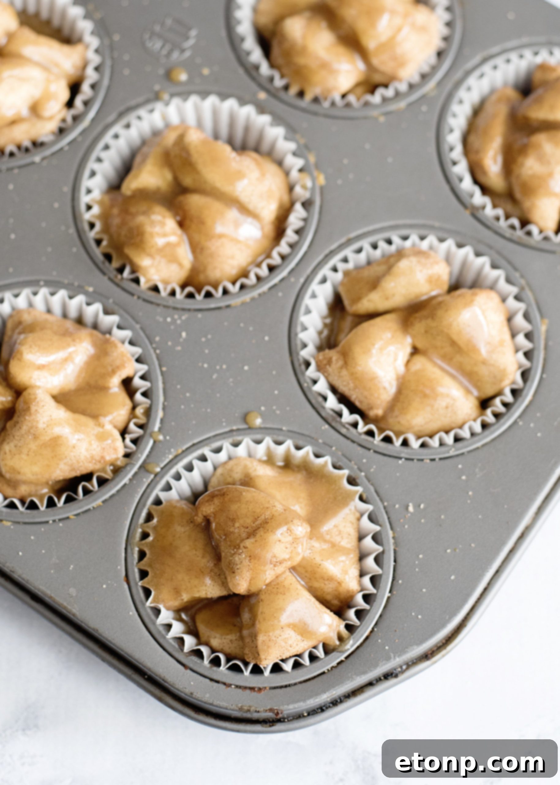 A bowl of granulated sugar mixed with cinnamon, with biscuit pieces ready for coating, highlighting the preparation step for Snickerdoodle Monkey Bread Muffins.