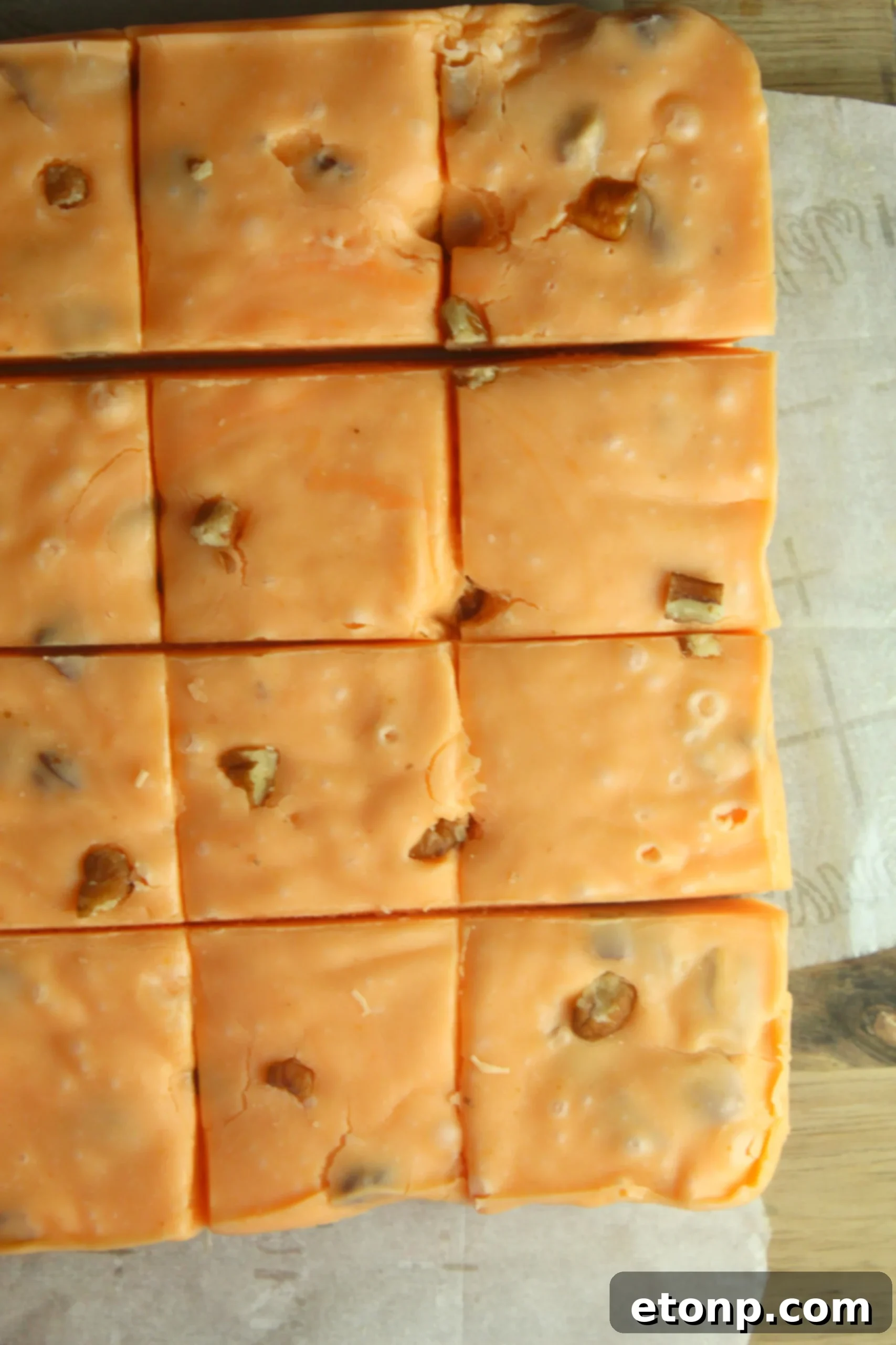 Hands holding a piece of pumpkin fudge with visible chopped pecans