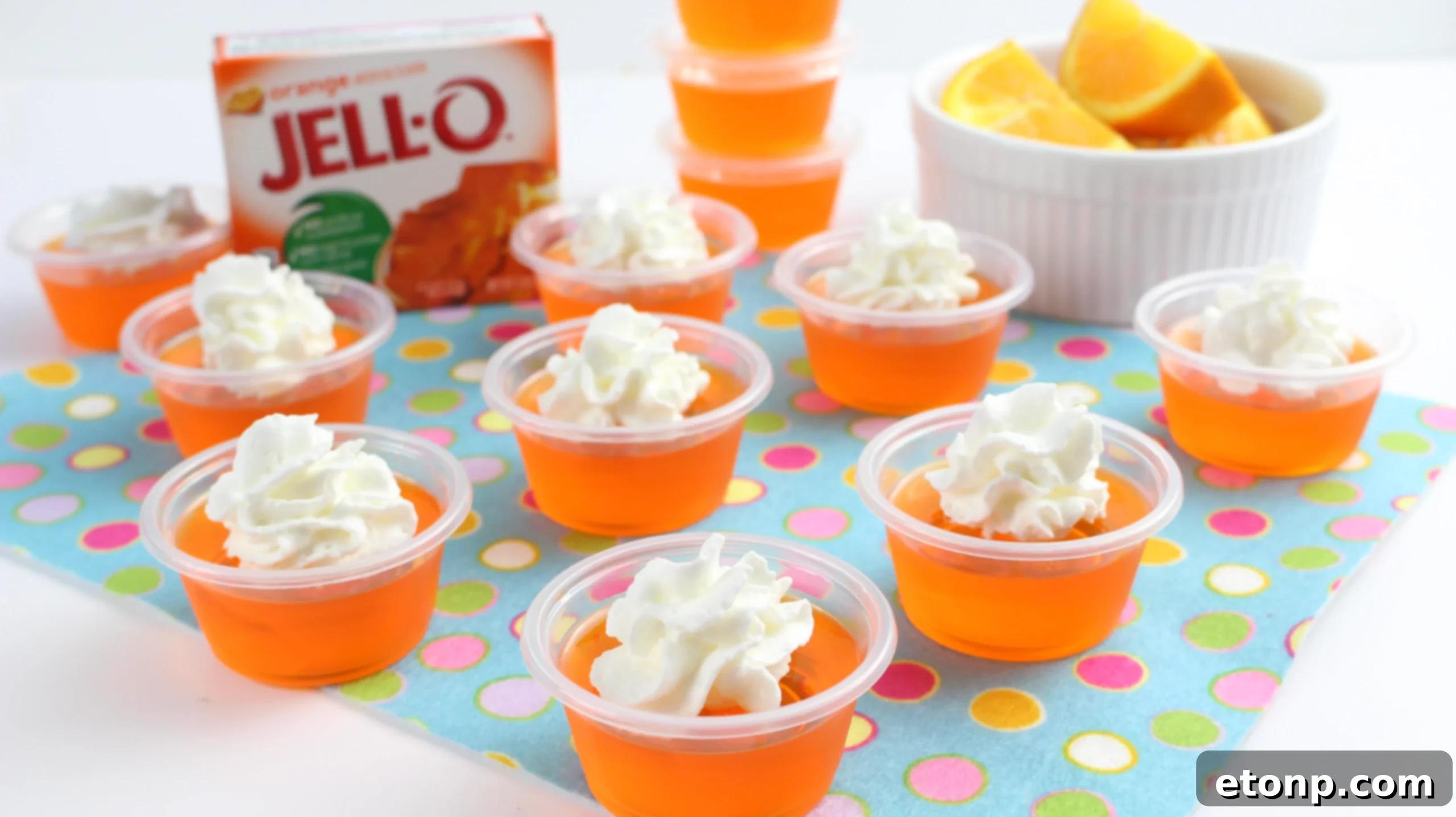 Hand holding an Orange Creamsicle Jello Shot with whipped cream, ready to be enjoyed at a social gathering.