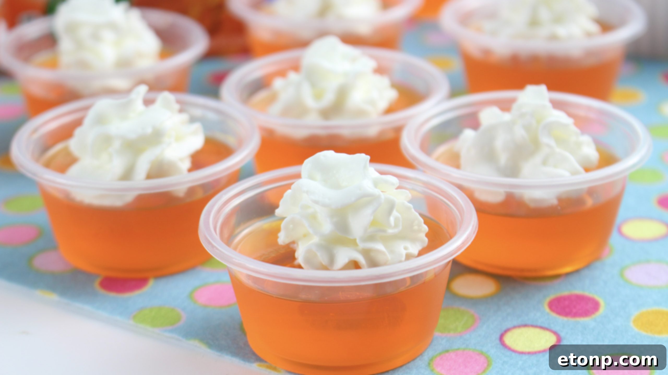 A close-up of a single Orange Creamsicle Jello Shot, focusing on the creamy whipped topping and smooth orange gelatin in a clear cup.