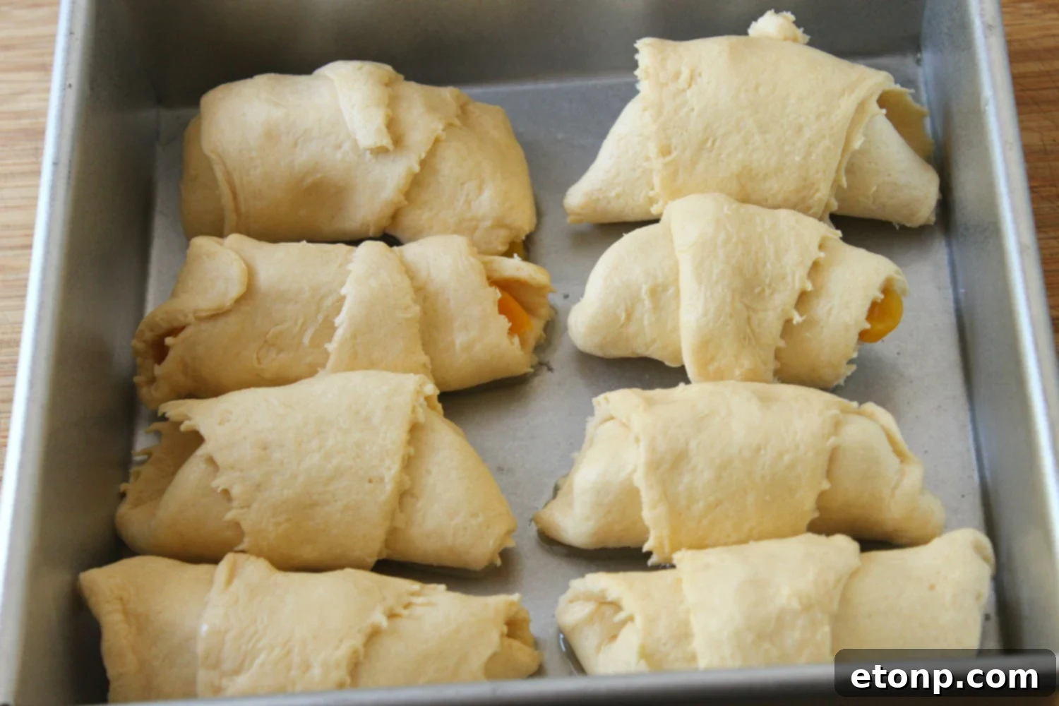 A hand placing fresh peach slices wrapped in crescent roll dough into a baking dish.
