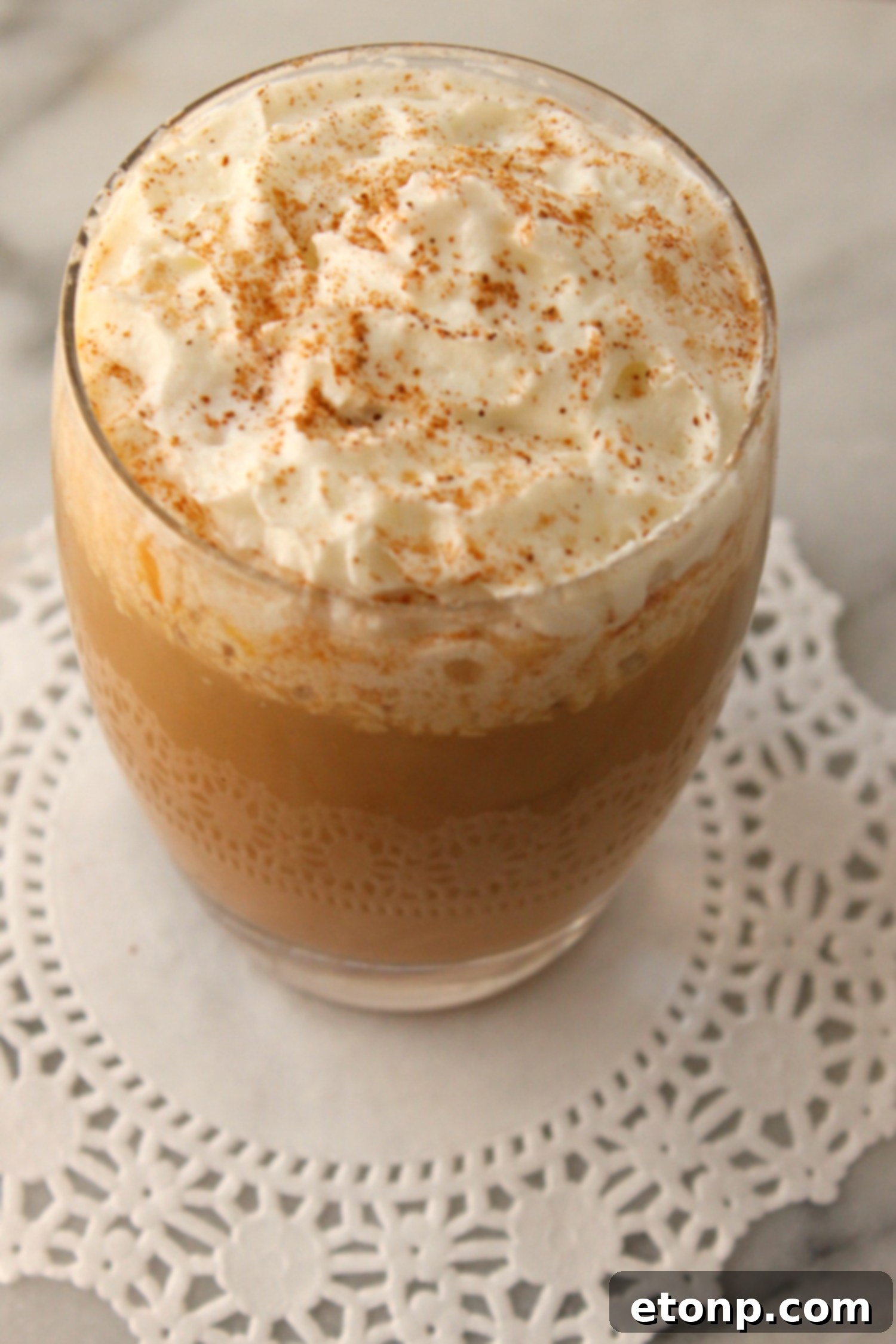 A steaming mug of coffee with homemade pumpkin spice creamer and whipped cream, sprinkled with pumpkin pie spice, on a cozy backdrop.