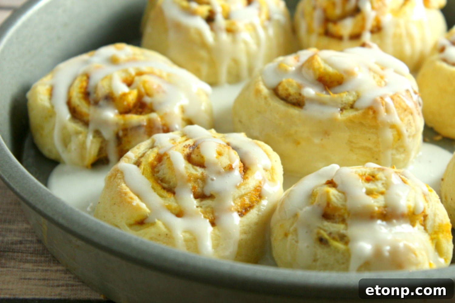 A plate of pumpkin cinnamon rolls topped generously with homemade cream cheese frosting and a sprinkle of spice, ready to be served.