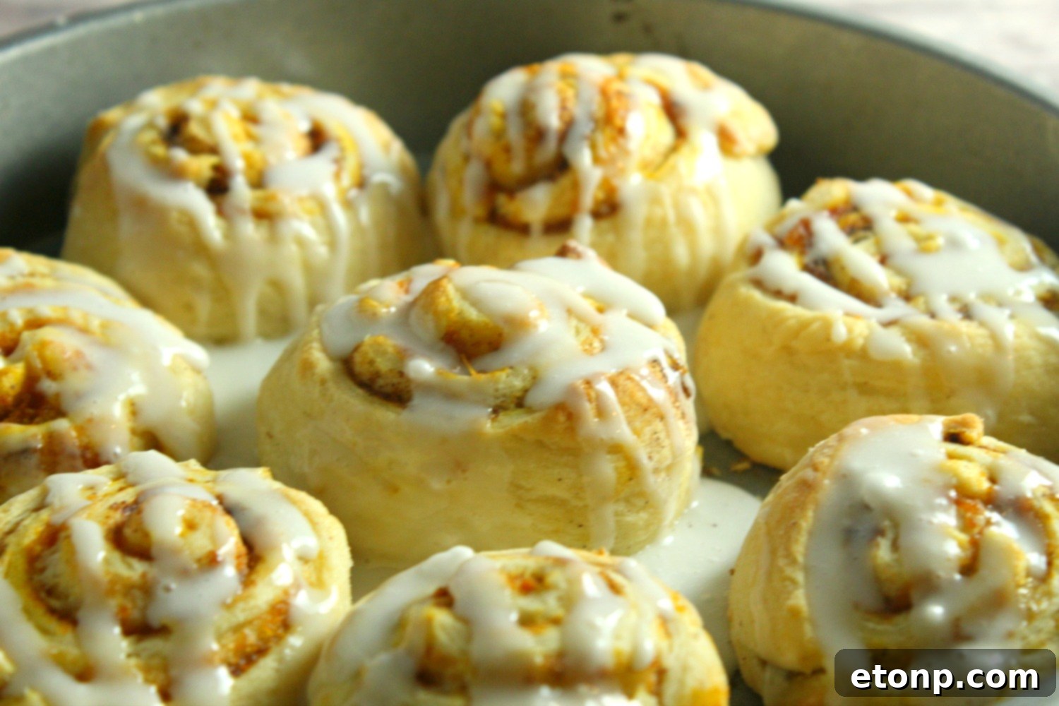 Two pumpkin cinnamon rolls on a rustic wooden plate, showcasing the thick, creamy cream cheese frosting and soft interior.