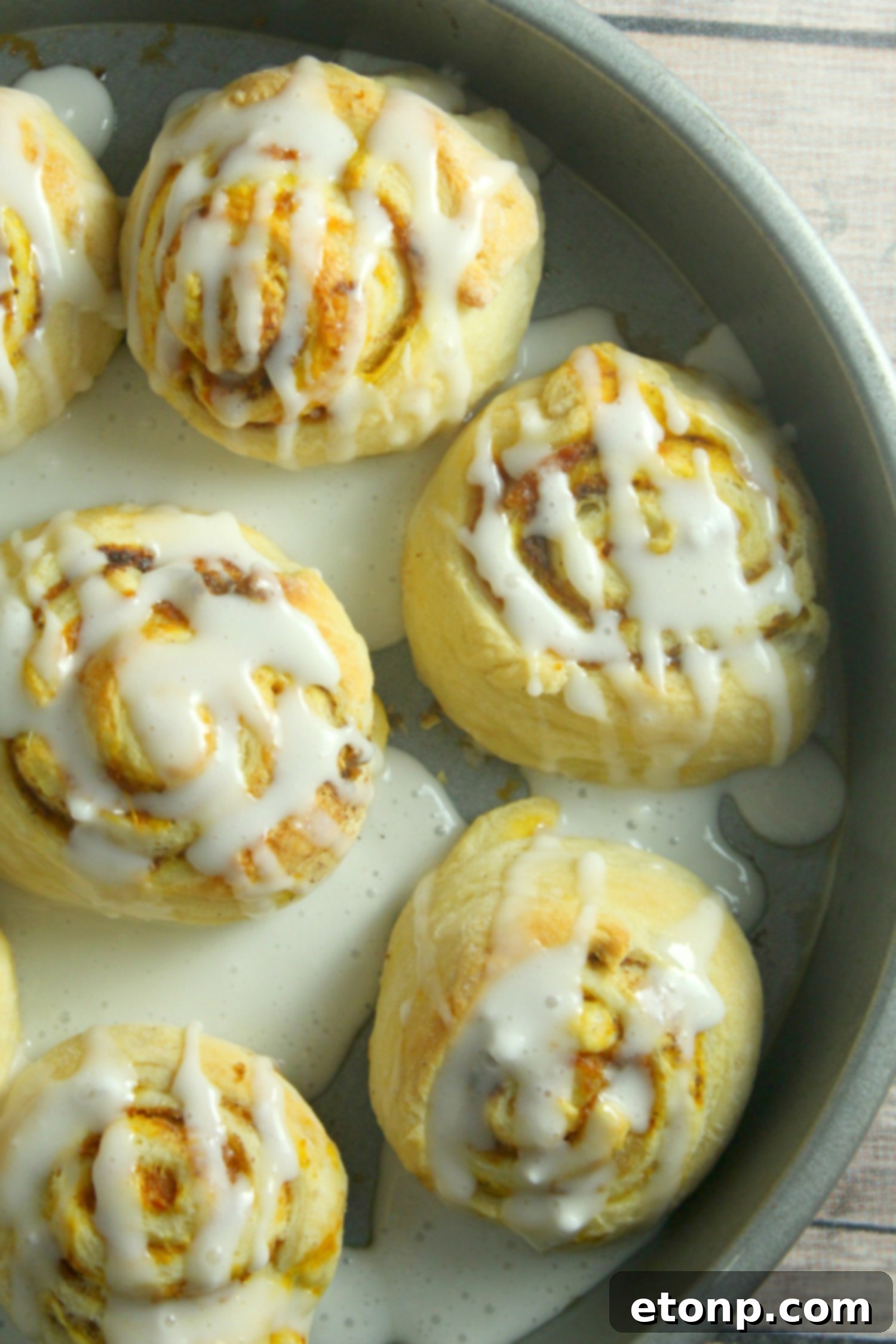 A single pumpkin cinnamon roll being lifted from a plate, highlighting its soft, gooey texture and generous frosting drizzle.
