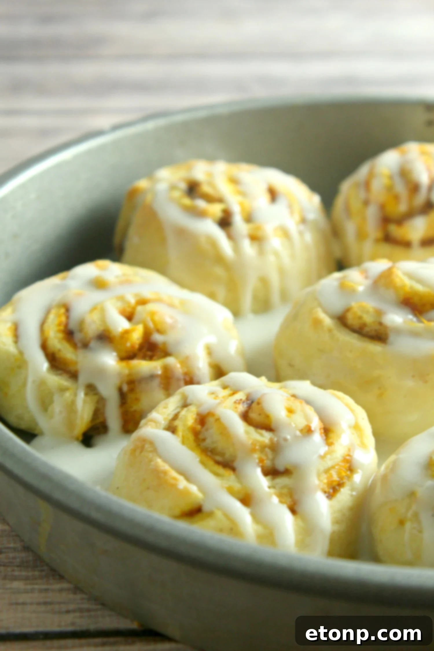 A stack of delicious pumpkin cinnamon rolls, fully frosted and sprinkled with extra pumpkin pie spice, ready to be devoured.