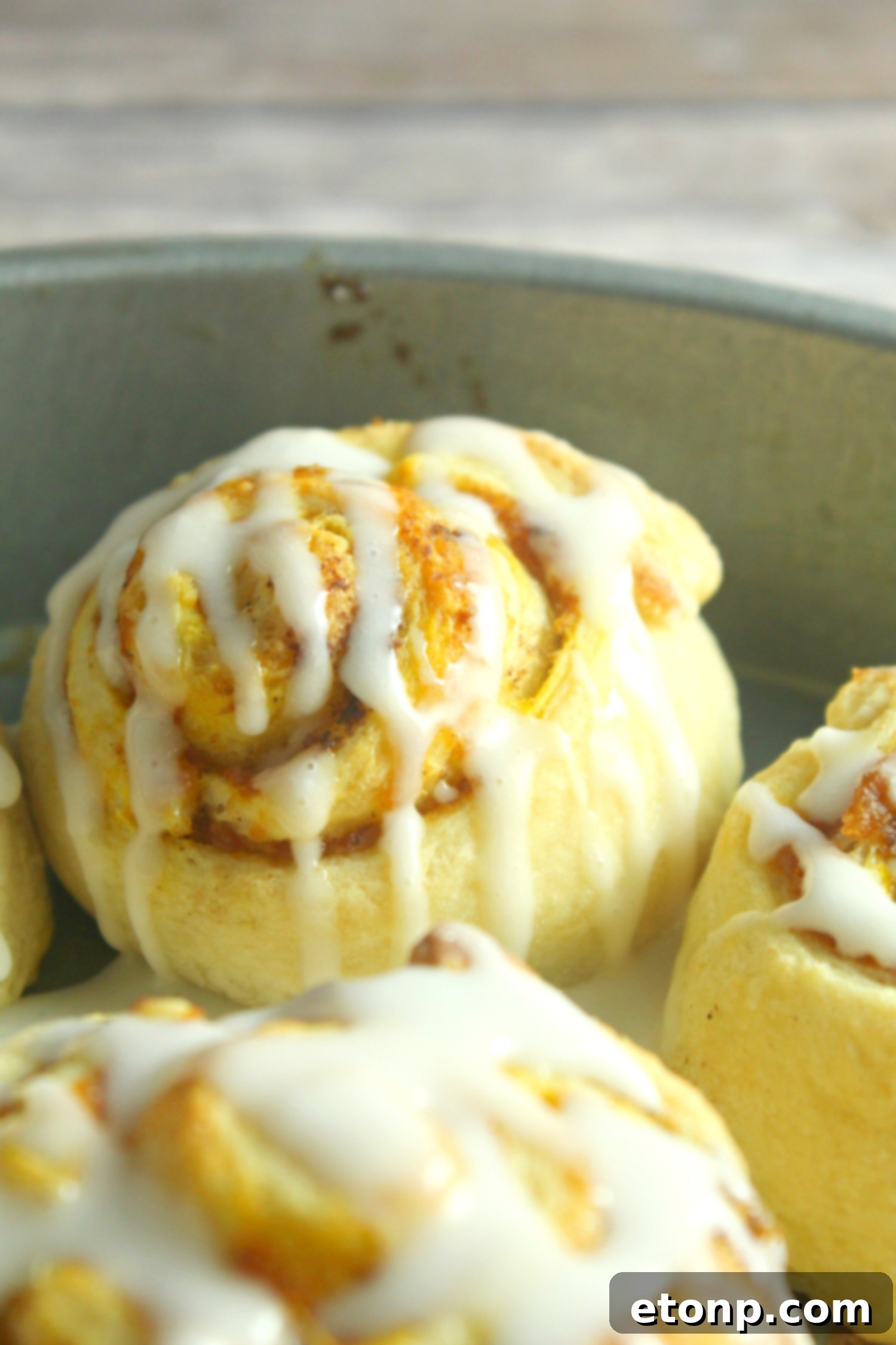 An overhead shot of multiple pumpkin cinnamon rolls covered in luscious cream cheese frosting, perfect for a festive fall treat.