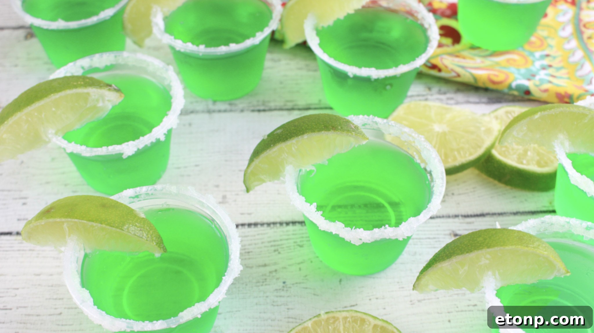 Margarita Jello Shots 3 Close-up shot of a single Margarita Jello Shot in a clear plastic cup, showcasing its vibrant green color and a perfectly sugared rim.