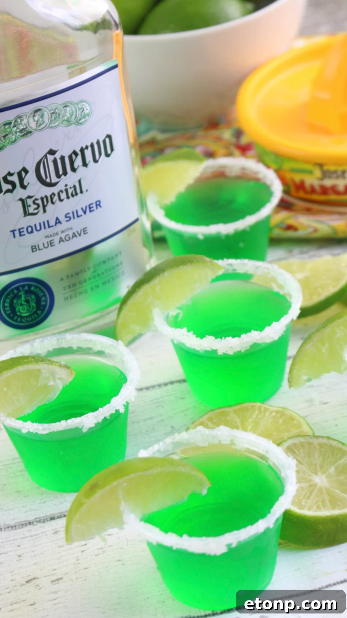 Margarita Jello Shots 5 Two hands preparing Margarita Jello Shots, one dipping a cup into lime juice and the other into margarita salt for perfect rimming.