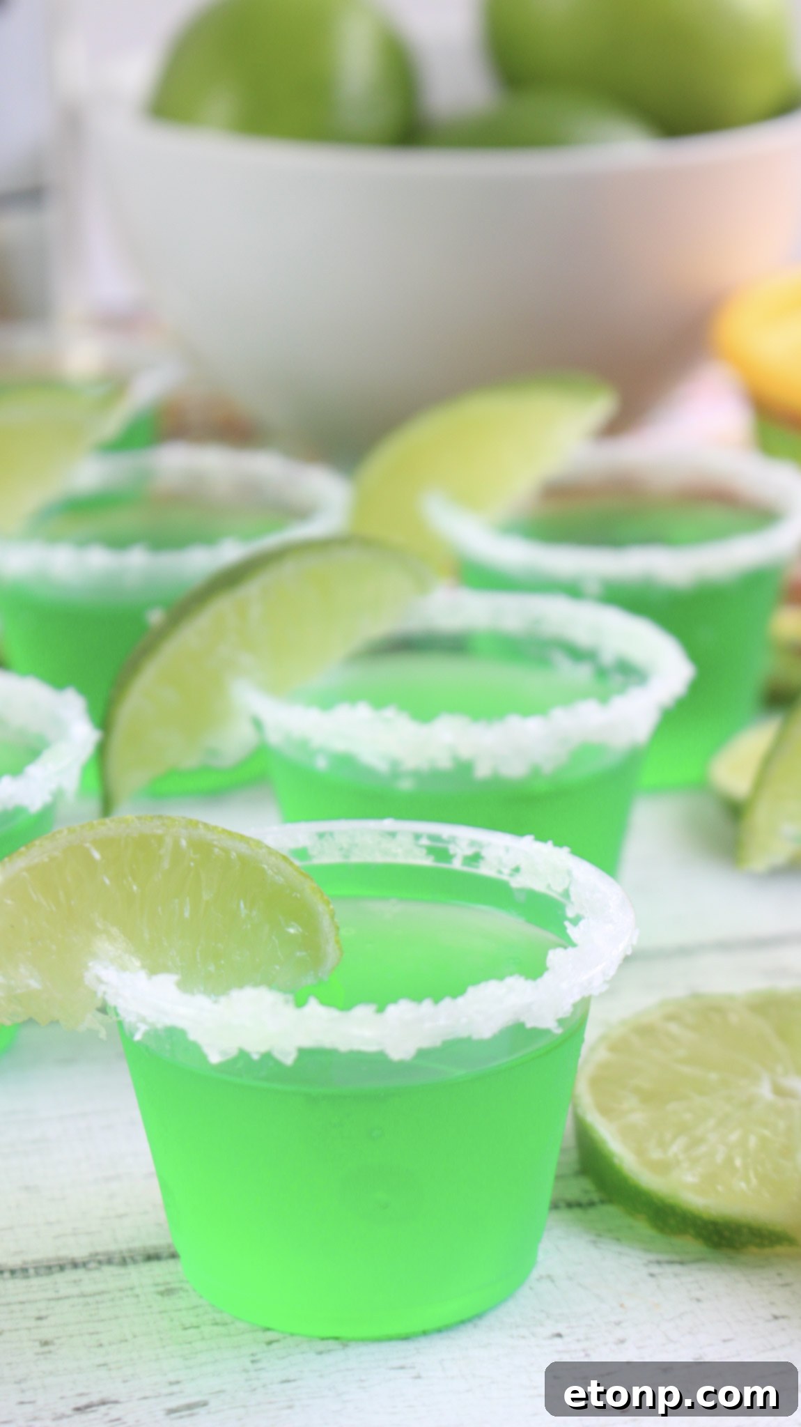 Margarita Jello Shots 7 Overhead shot of freshly made Margarita Jello Shots in mini plastic cups with lime wedges and a few loose lime slices.