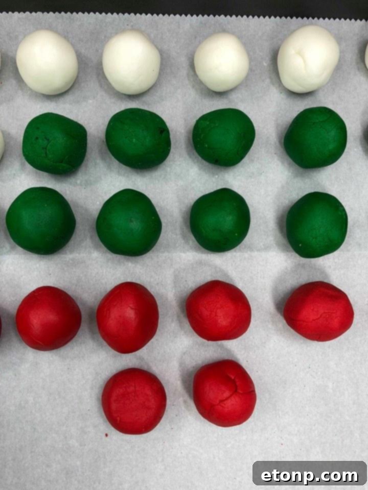 Child's hands rolling a colorful peppermint patty dough ball in granulated sugar.