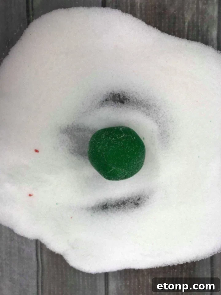 A hand gently flattening a sugar-coated peppermint patty ball with a fork.