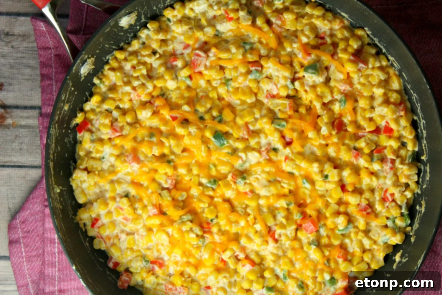 Overhead shot of the hot corn dip in a cast iron skillet, surrounded by colorful ingredients like bell peppers and jalapeños.