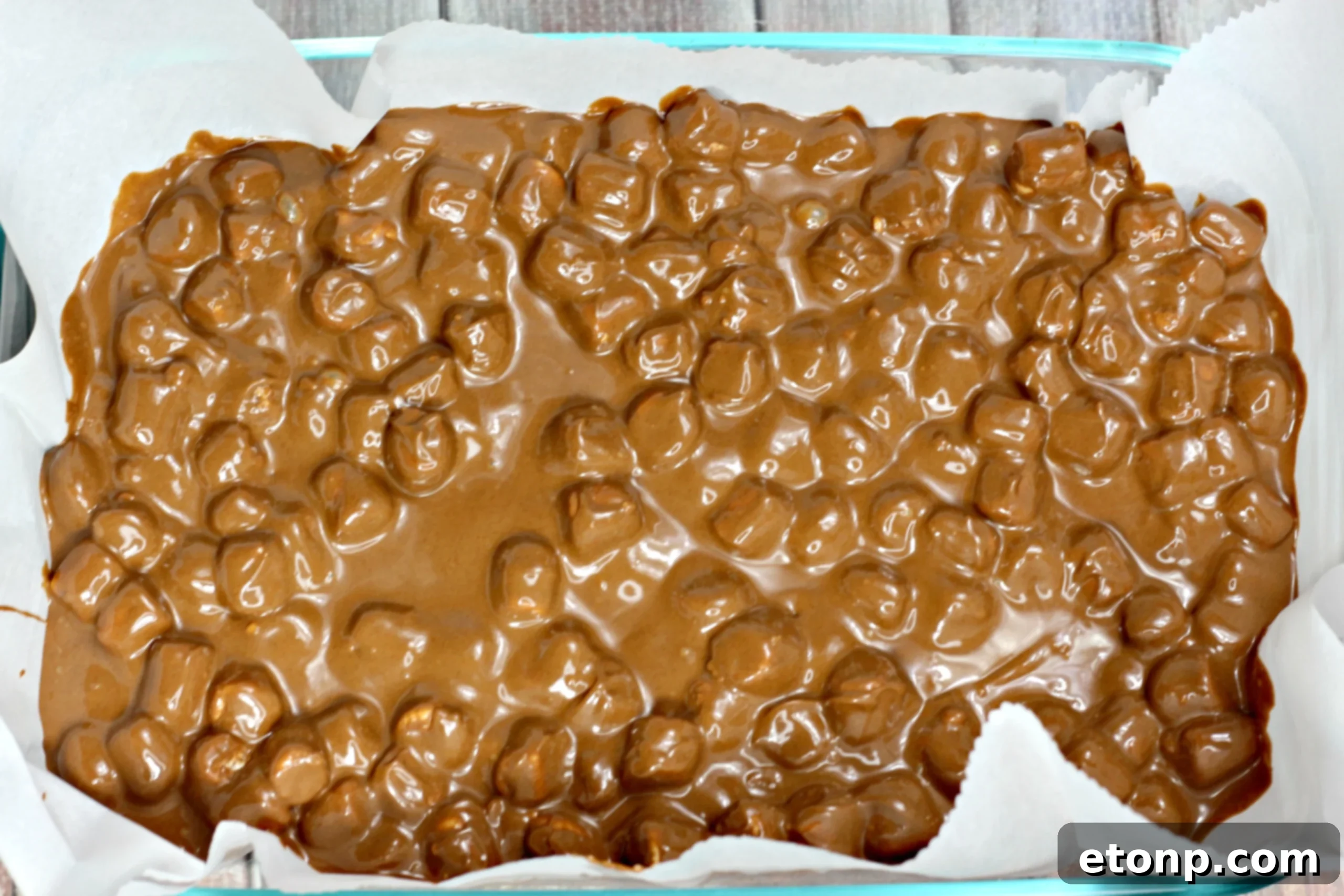 Marshmallow chocolate mixture being spread evenly into a parchment-lined baking pan.