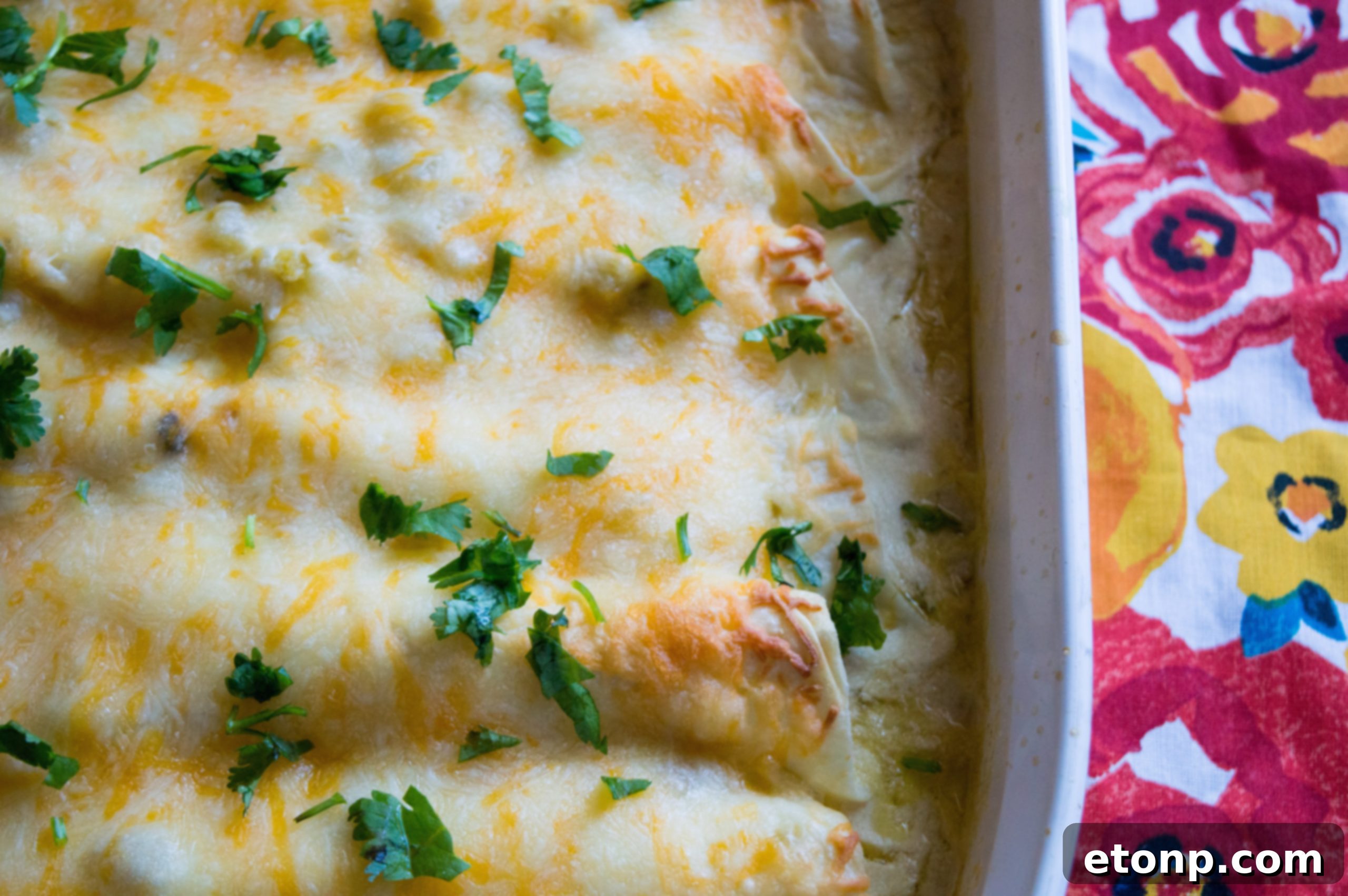 A casserole dish filled with White Chicken Enchiladas generously topped with an assortment of melted cheeses