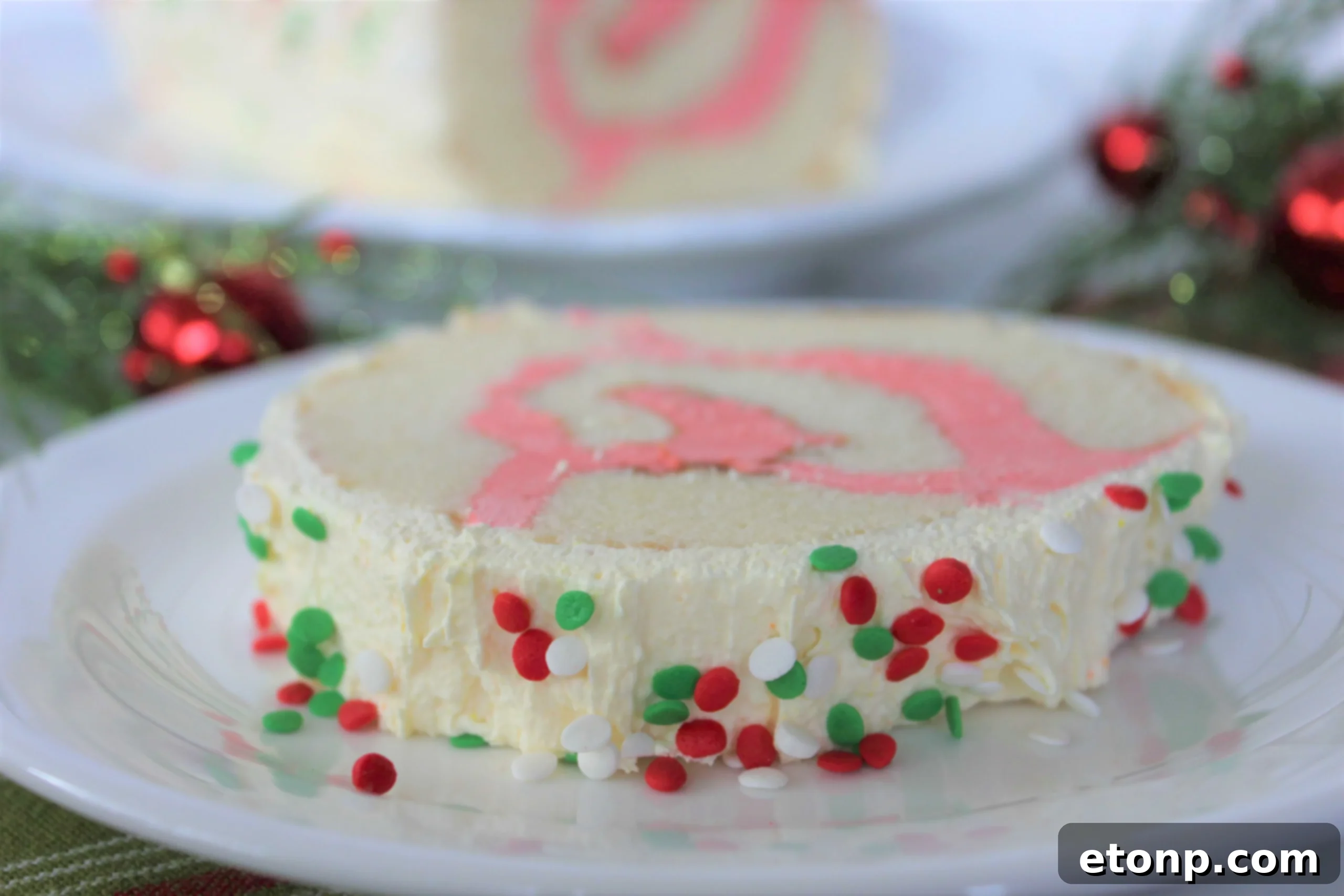 Christmas Cake Roll Made Easy 3 Close-up of the Christmas Cake Roll, showcasing the smooth, white frosting and the vibrant red swirl of the filling.