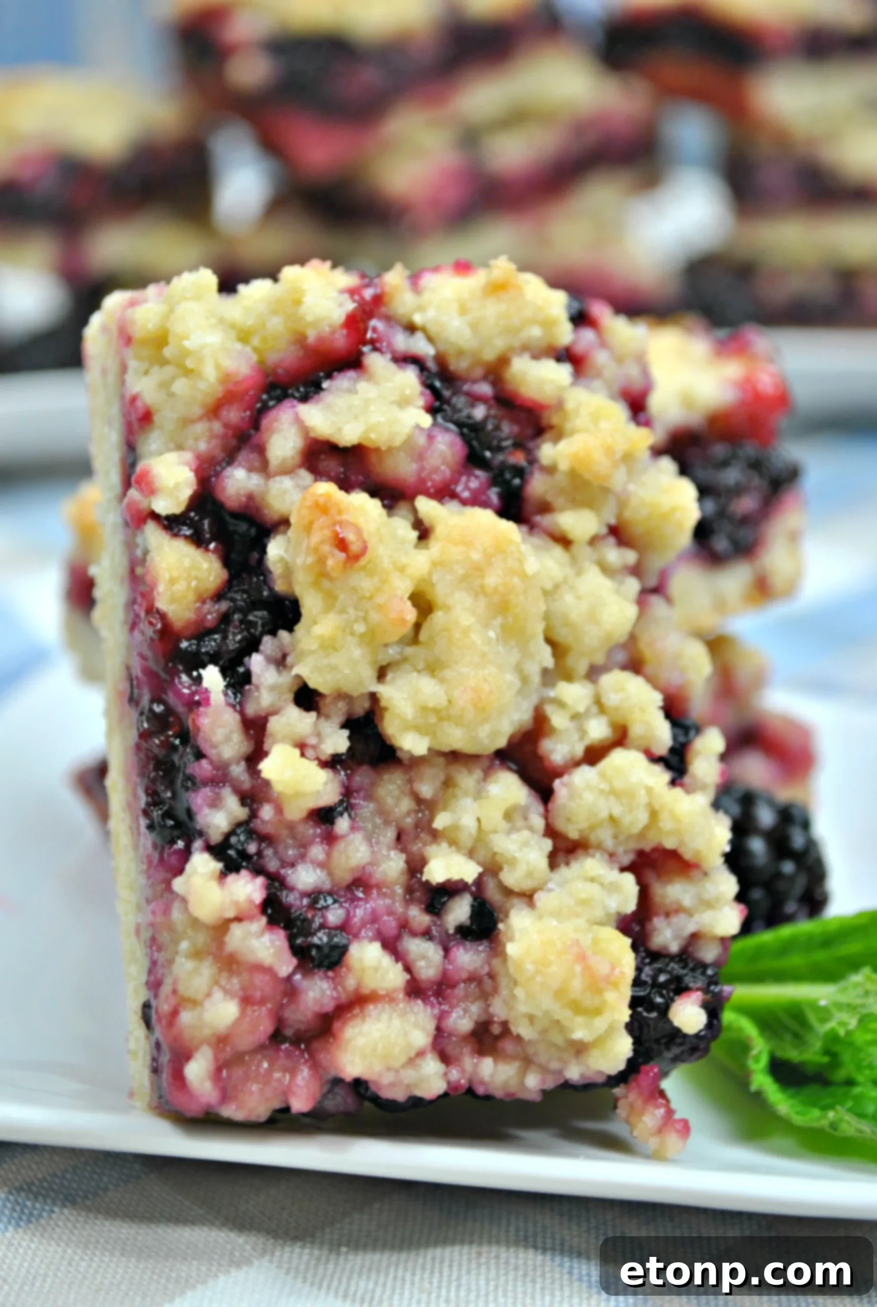 A hand reaching for a blackberry pie crumble bar, emphasizing the ease of eating this dessert without utensils.