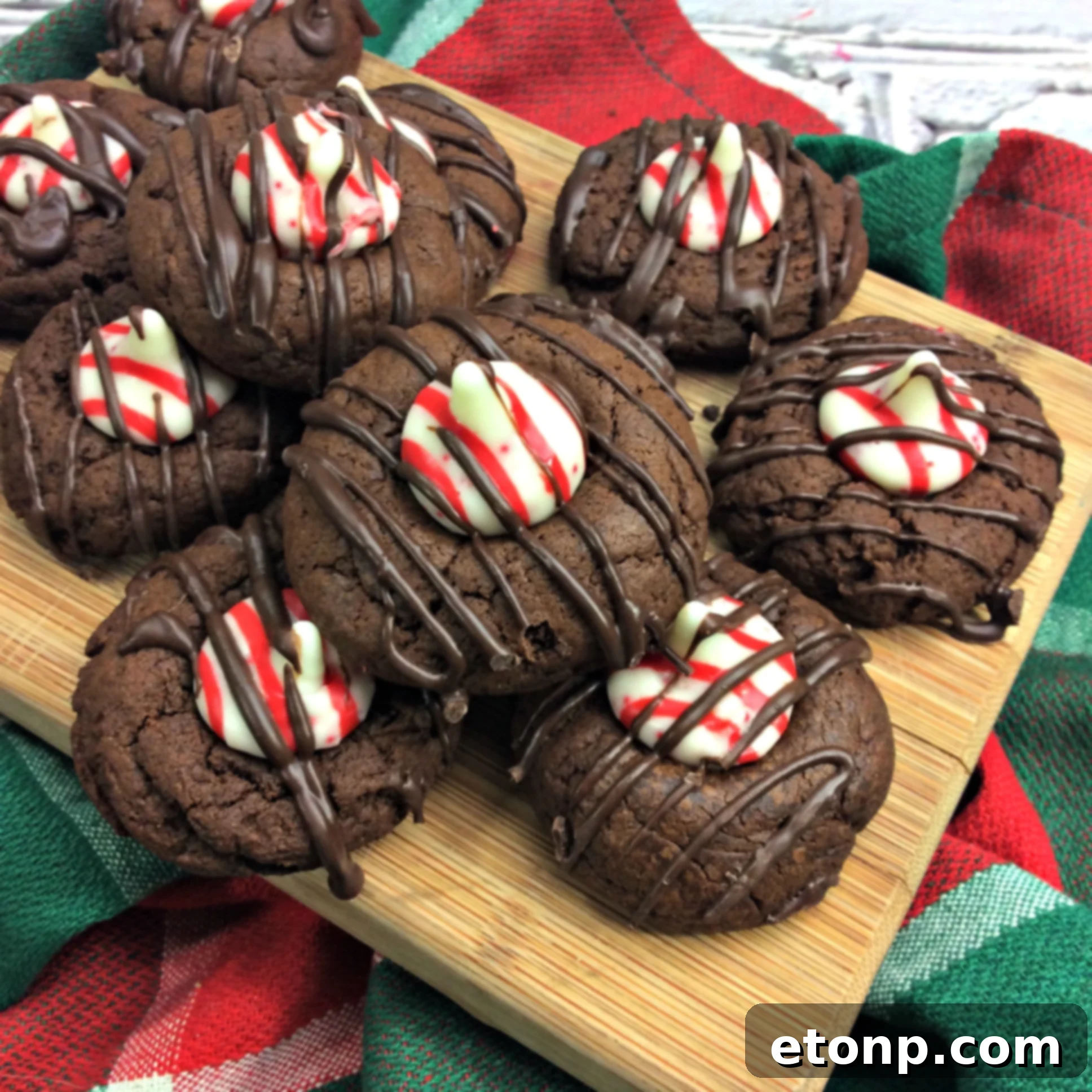 A stack of three chocolate peppermint thumbprint cookies on a rustic wooden surface, garnished with fresh mint.