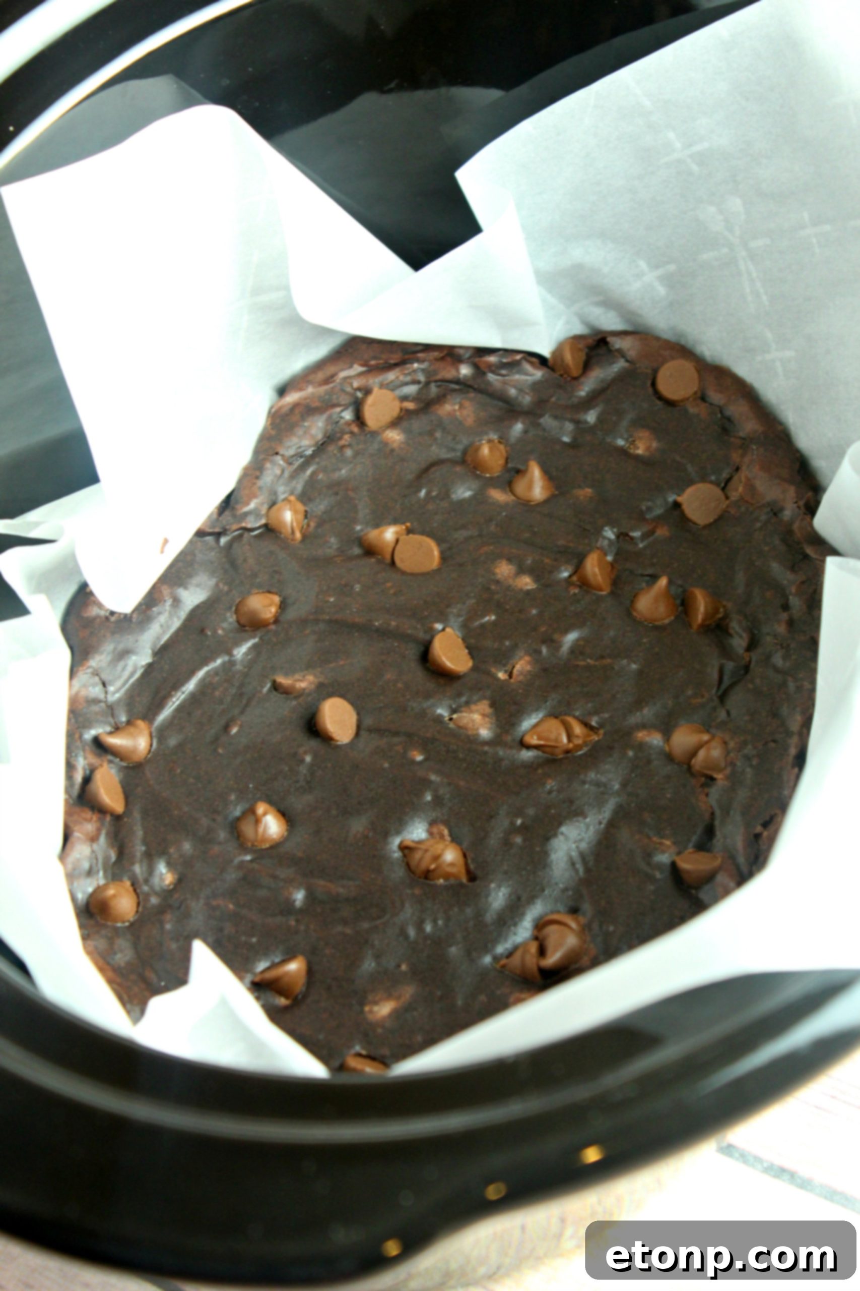 Interior of a slow cooker pot meticulously lined with parchment paper, prepared for brownie batter