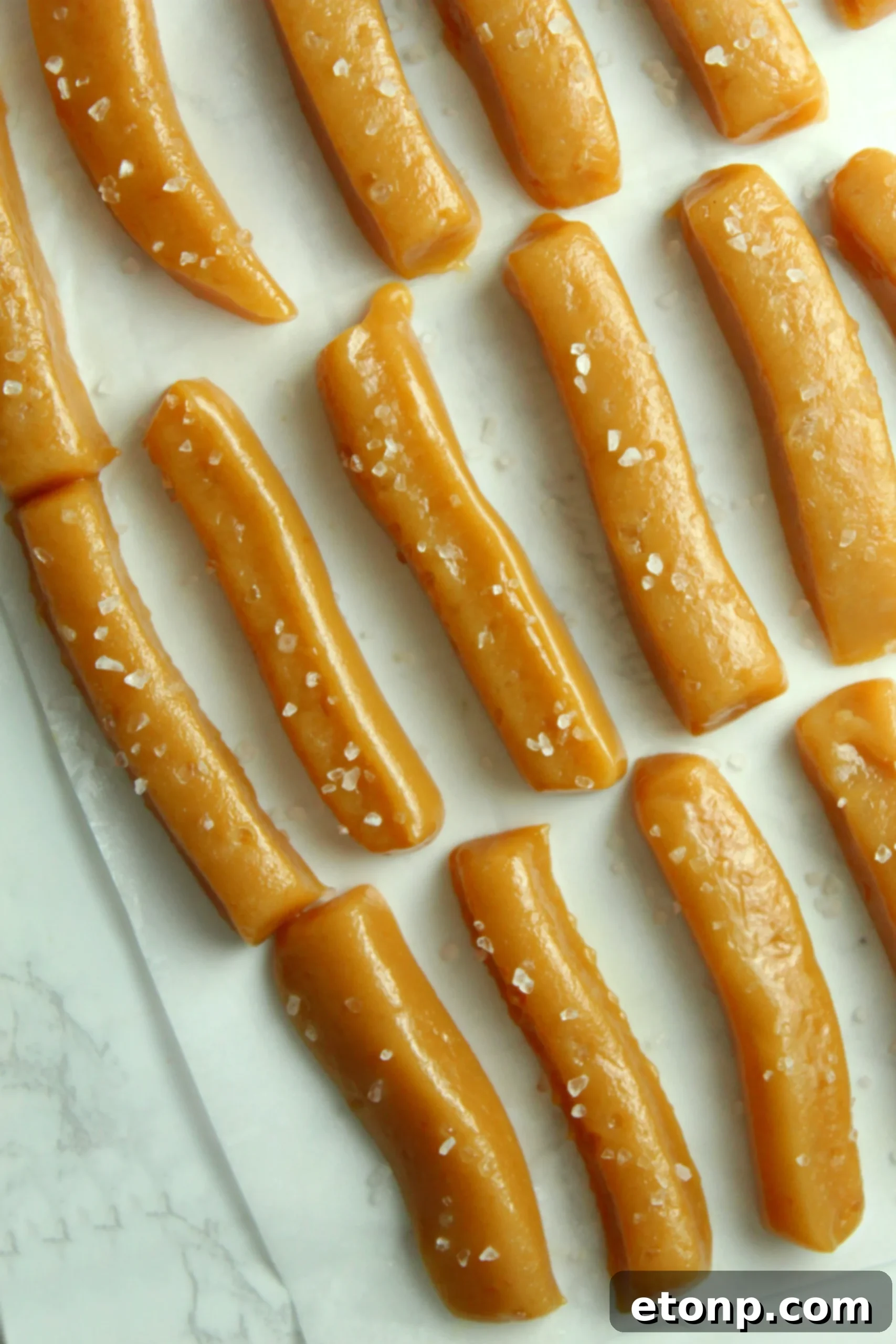 A hand holding a piece of unwrapped salted caramel, emphasizing its soft and appealing texture.