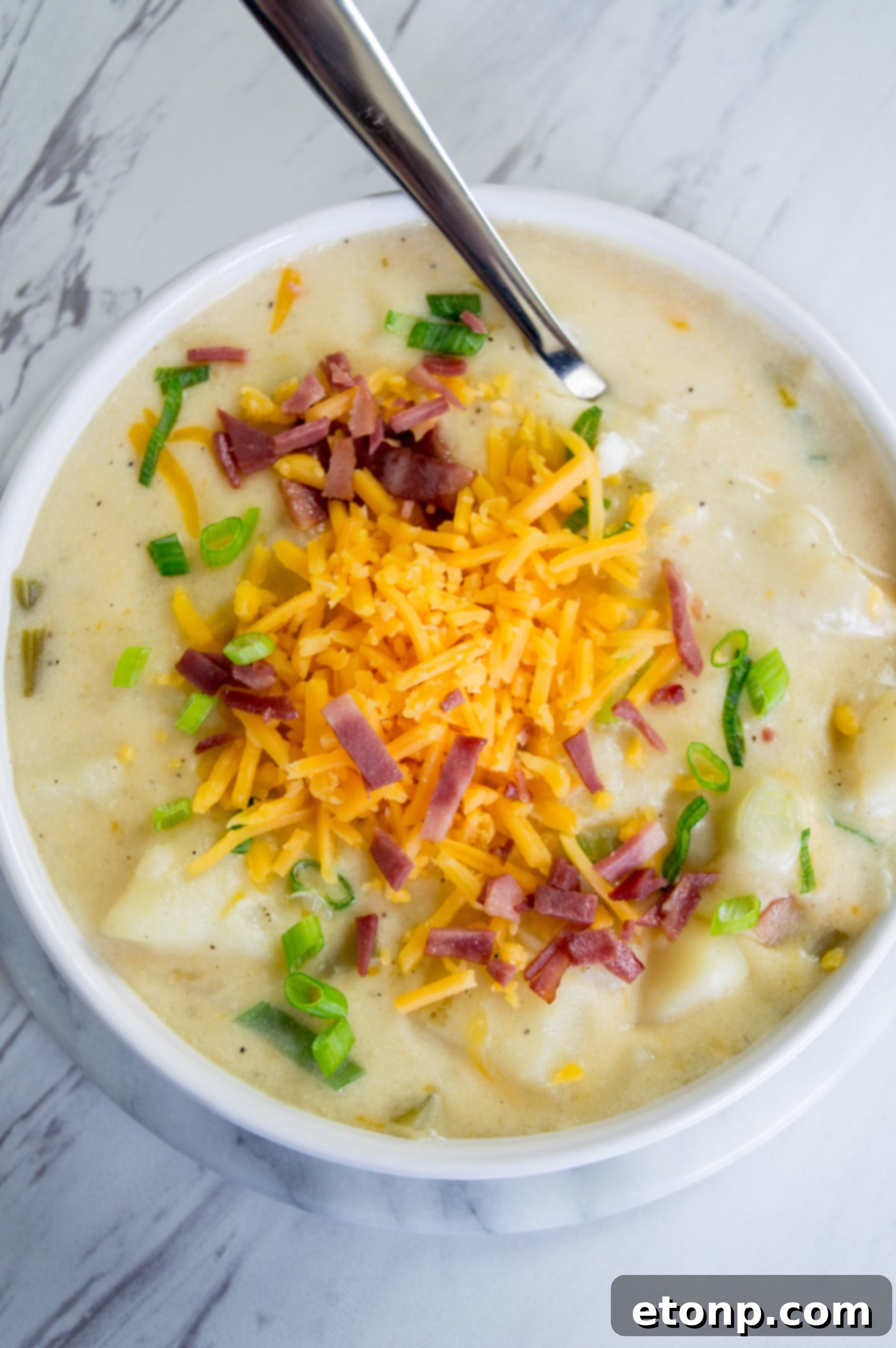 Ultimate Comfort Potato Soup 4 A close-up of a spoon dipping into a thick, creamy potato soup, showing melted cheese and potato chunks.