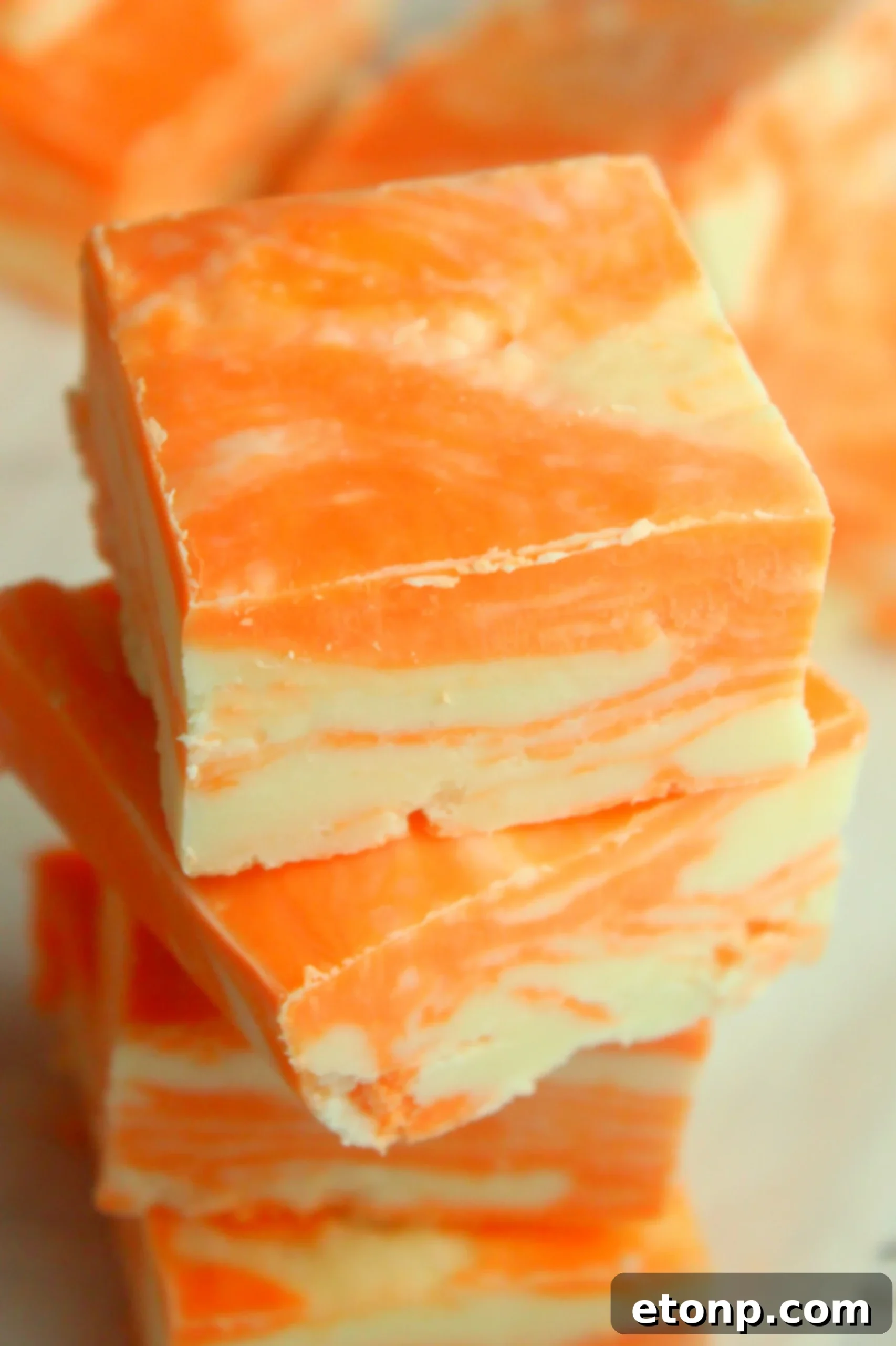 Easy No Bake Orange Creamsicle Fudge 7 Close-up of a stack of orange creamsicle fudge squares, showing the creamy texture and swirl.