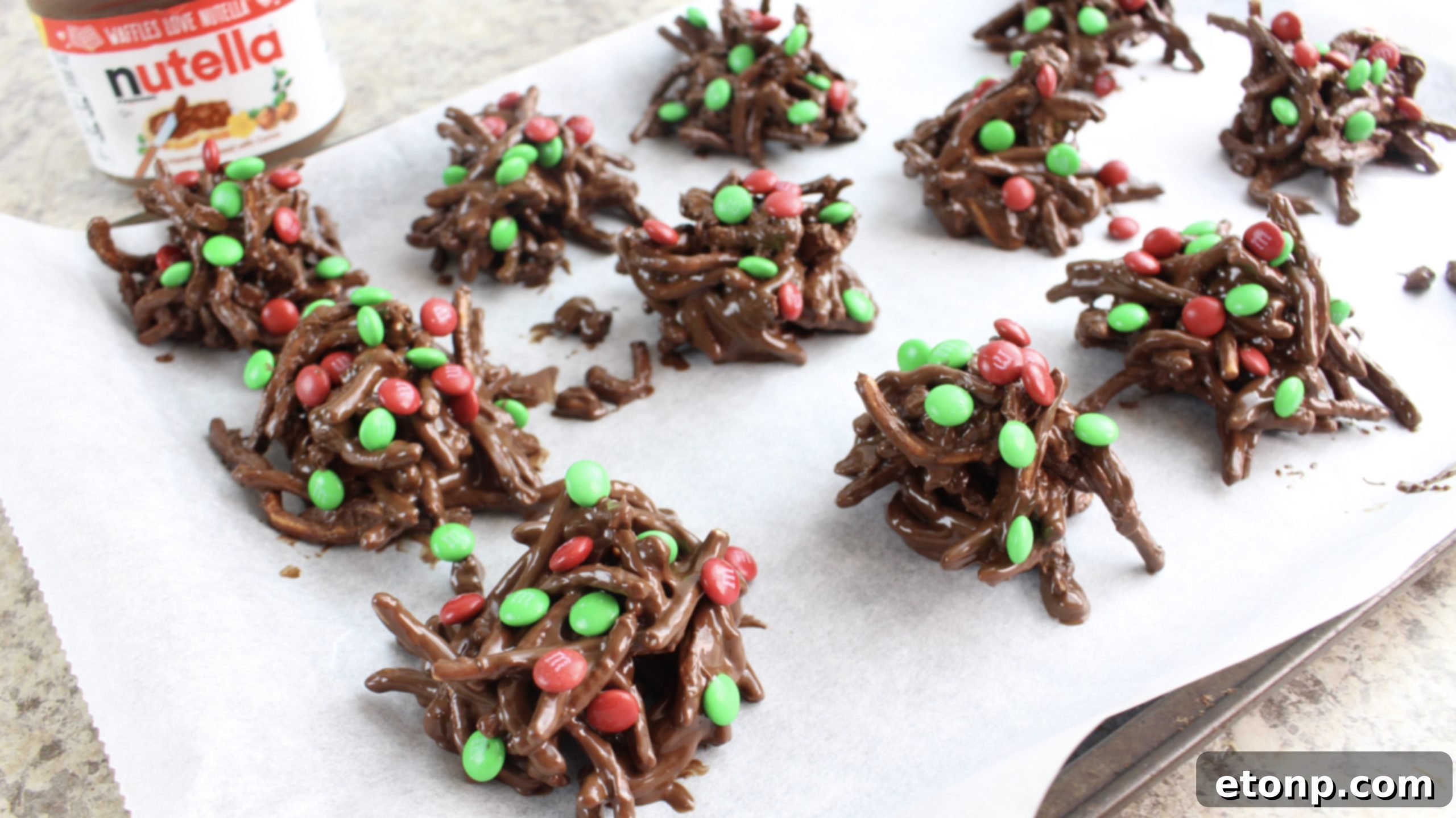 Spoonfuls of chocolate haystack mixture being dropped onto parchment paper on a baking sheet.