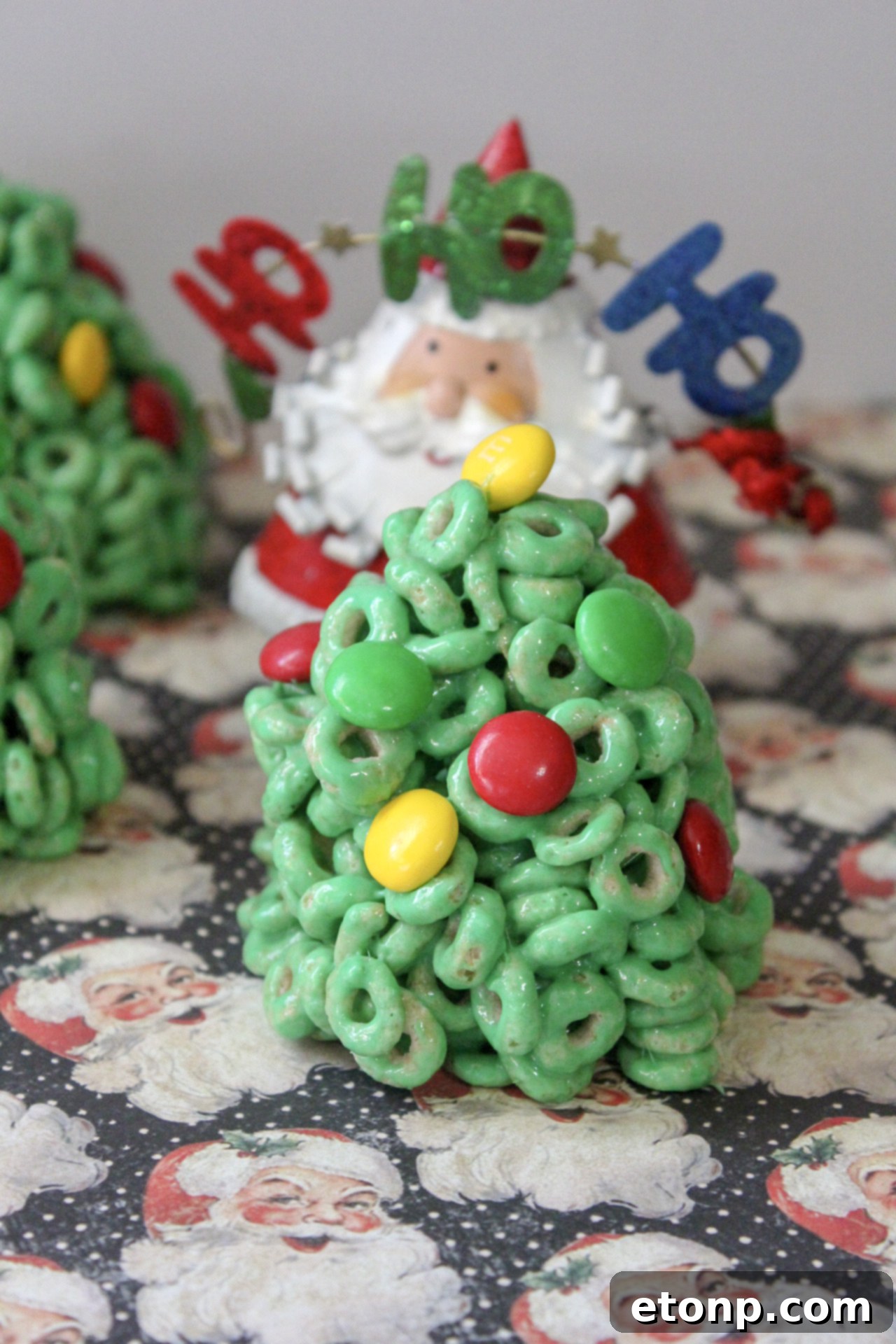 A close-up of green Cheerio treats shaped like Christmas trees, decorated with M&Ms.