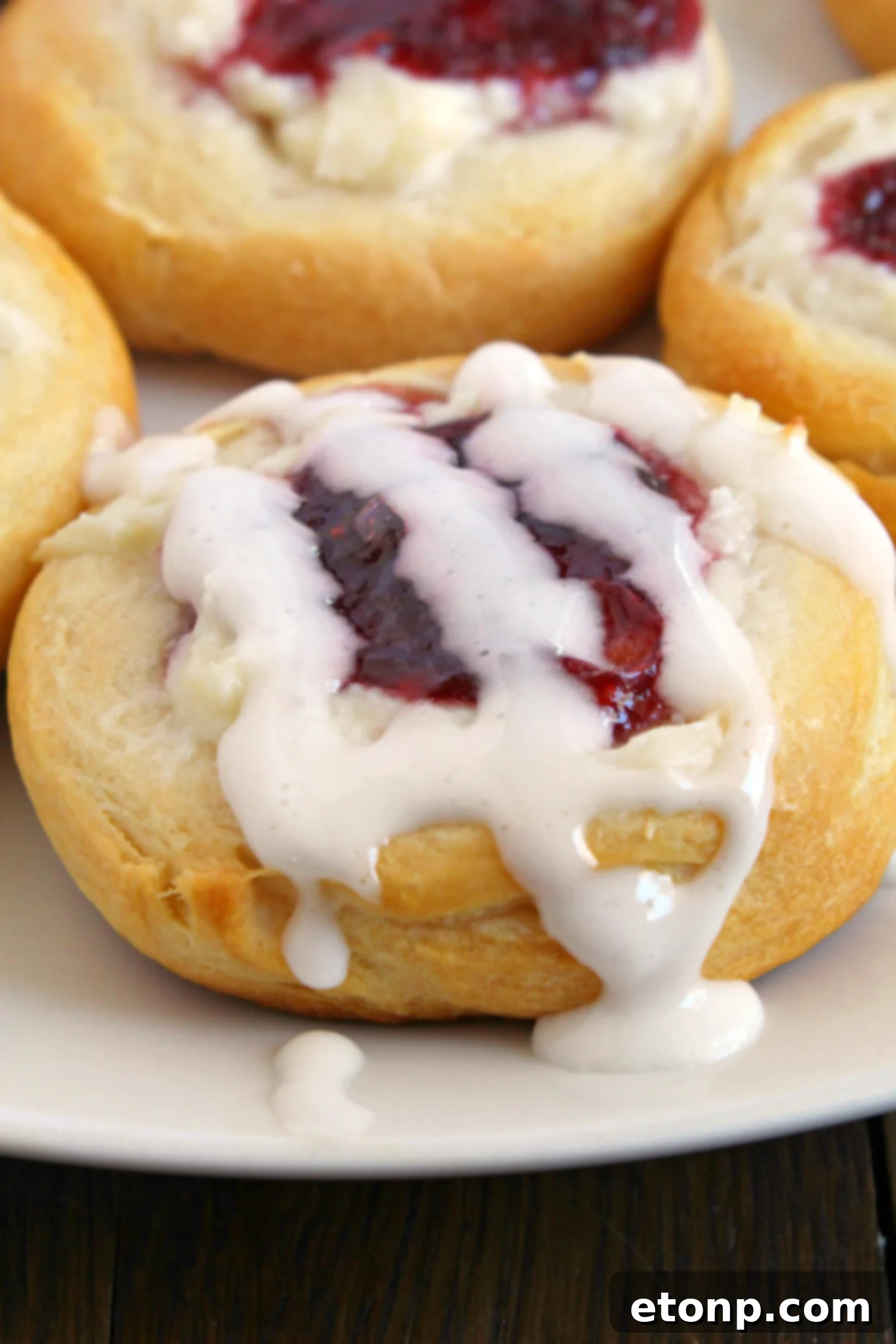 Luscious Raspberry Cream Cheese Crescents 5 A close-up of a Raspberry Cream Cheese Crescent Danish drizzled with white glaze, highlighting the texture and glistening surface.