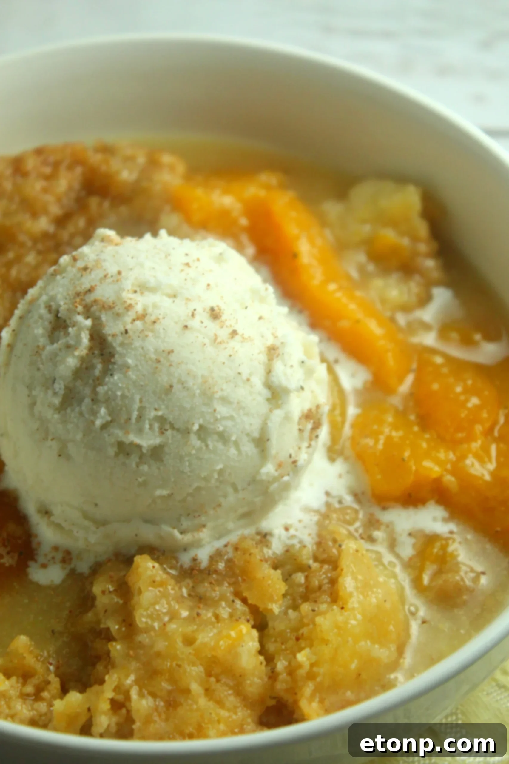 Delicious Slow Cooker Peach Cobbler ready to be served, topped with vanilla ice cream