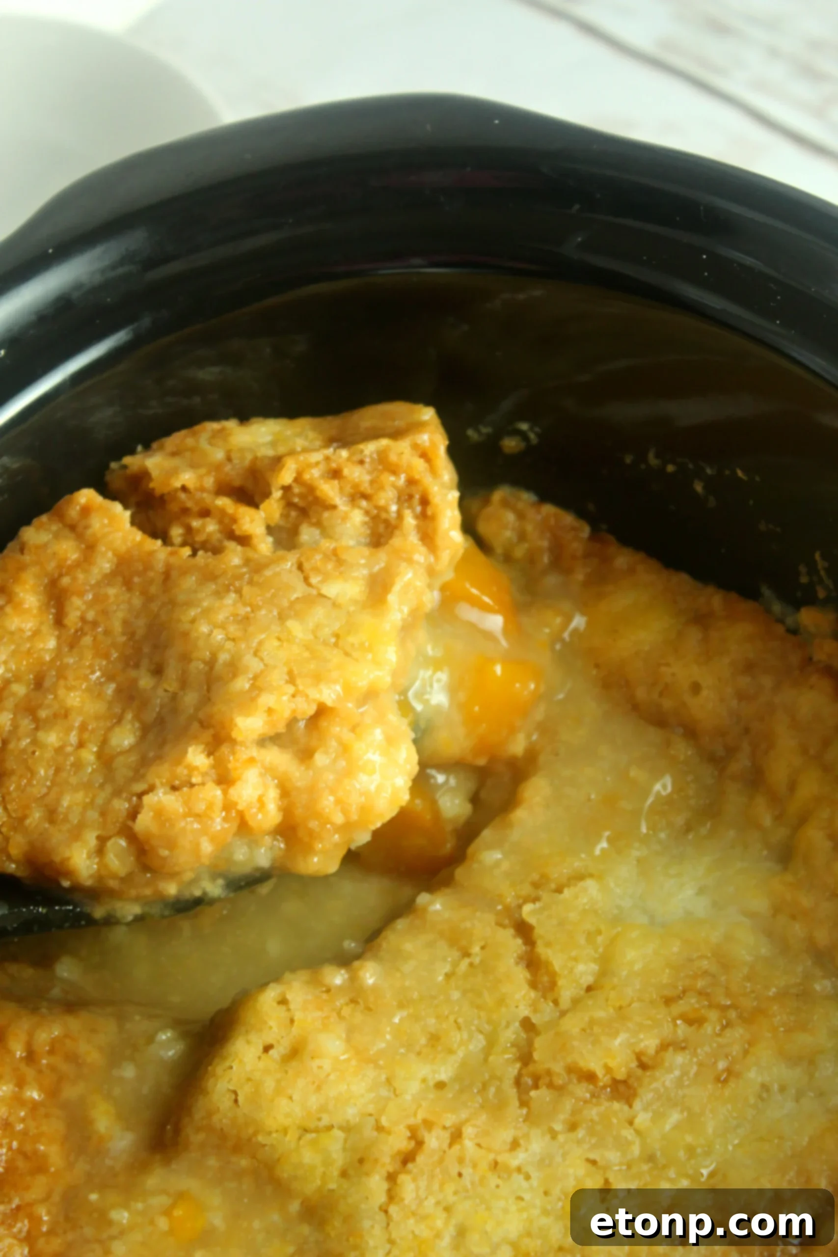 A close-up of a single serving of peach cobbler, showing the fruit and cake topping with melted ice cream