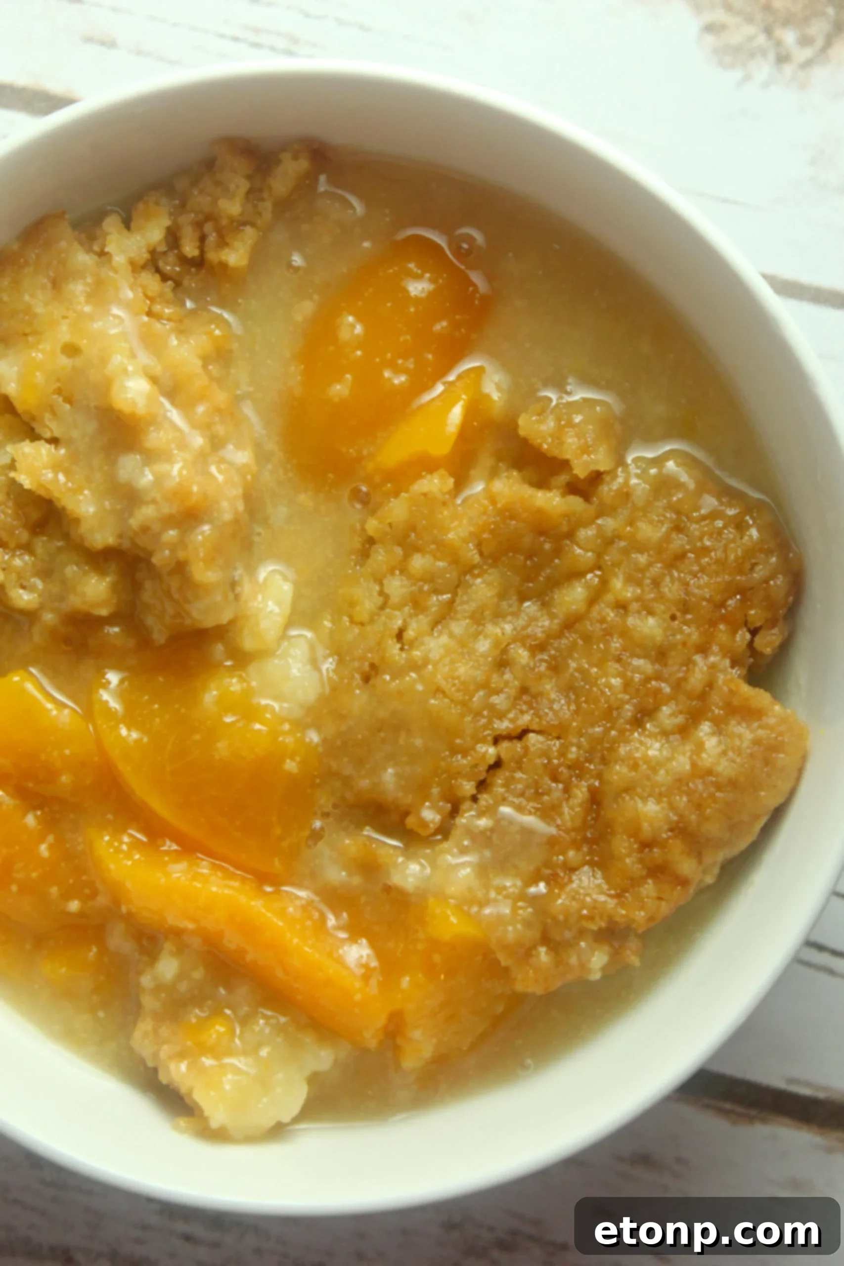 A full slow cooker peach cobbler, glistening and warm, with a serving spoon nestled within