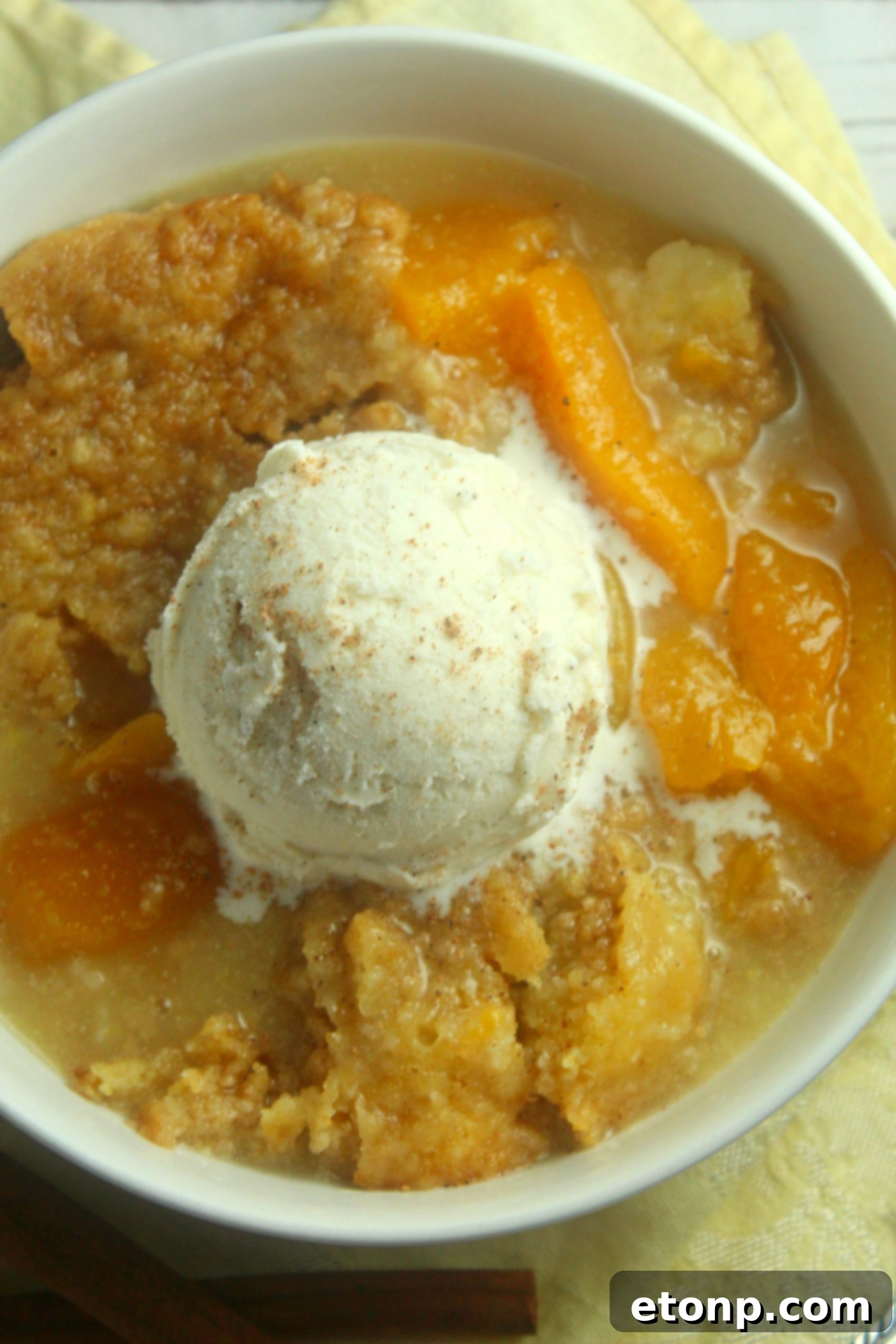 Multiple servings of warm slow cooker peach cobbler in bowls, topped with vanilla ice cream and cinnamon