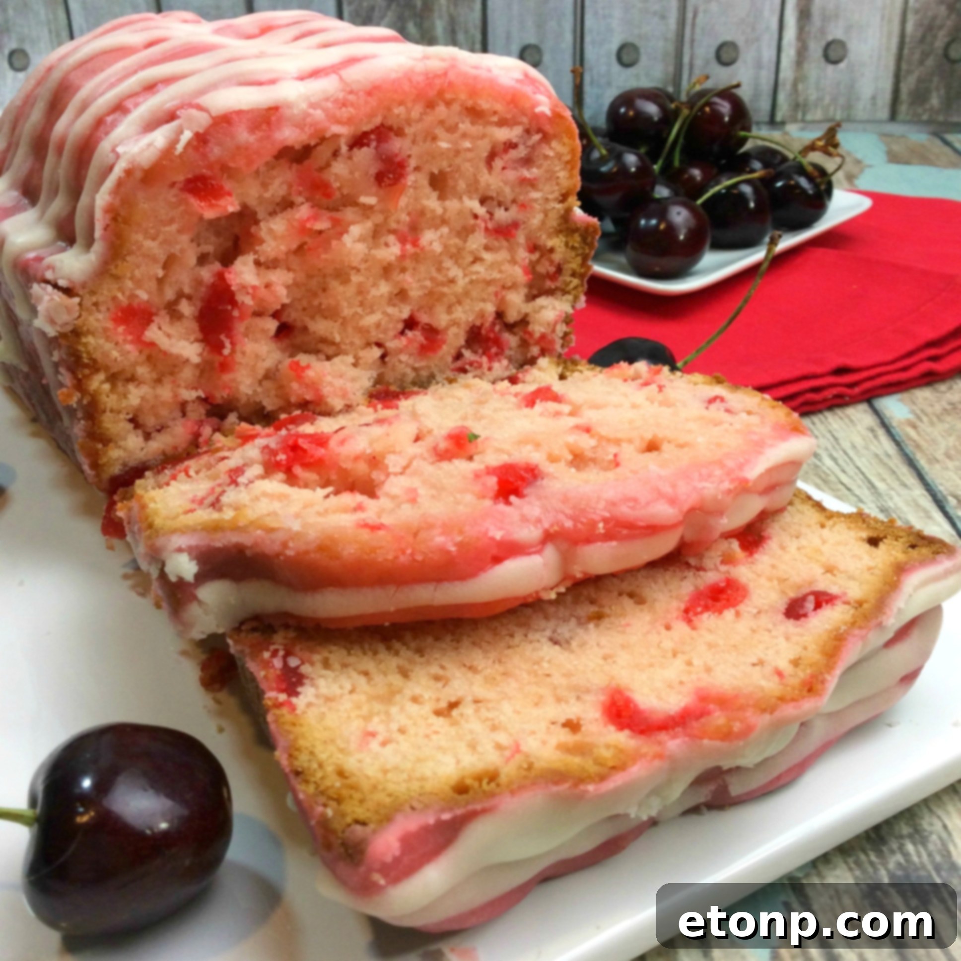 A beautifully sliced Cherry Garcia Loaf Cake, showing the vibrant red cherries throughout the moist cake, topped with a luscious pink cherry glaze.