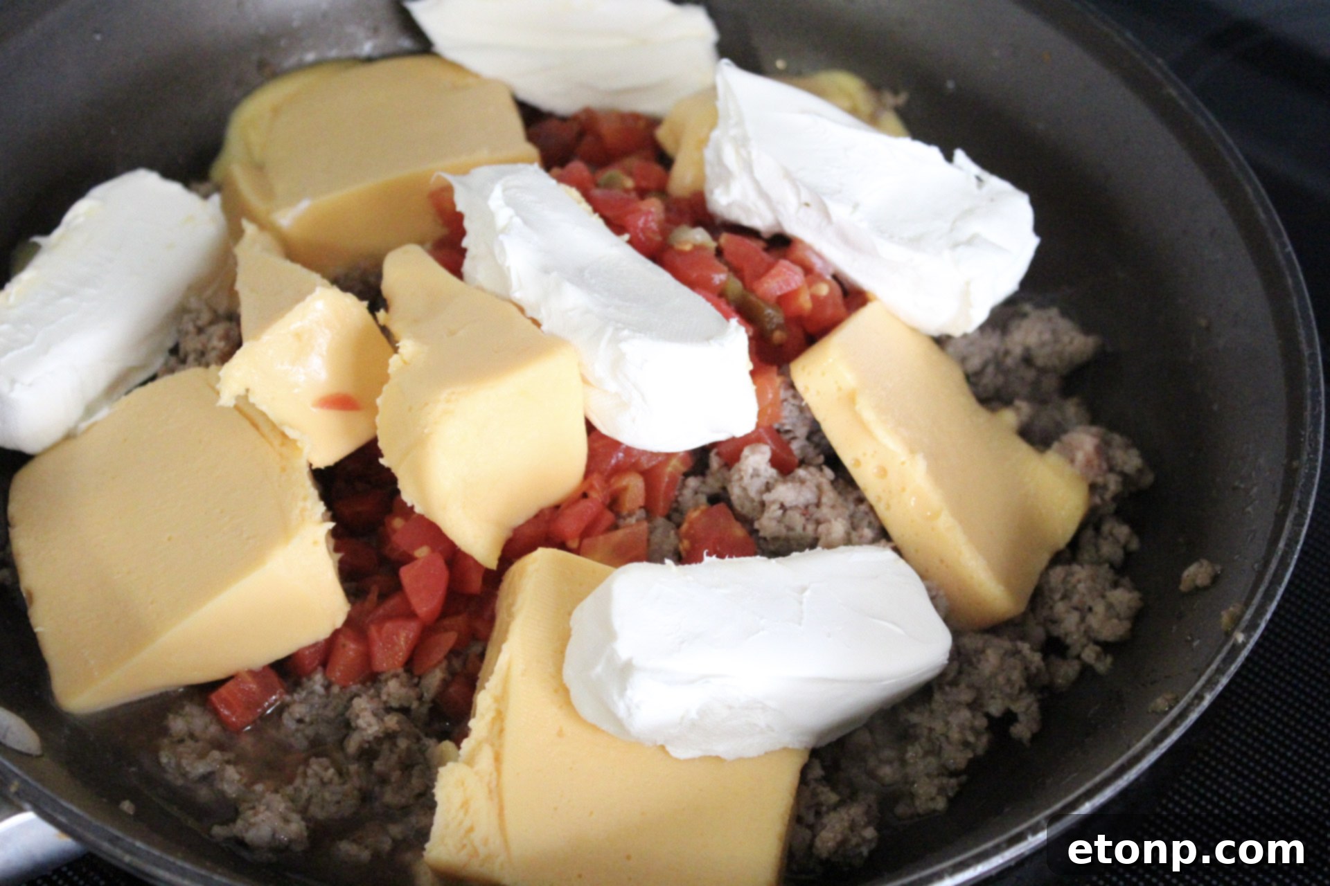 Close-up shot of the three main ingredients for the cheesy sausage dip: a block of Velveeta-style cheese, a package of cream cheese, and a can of Rotel diced tomatoes and green chilies.