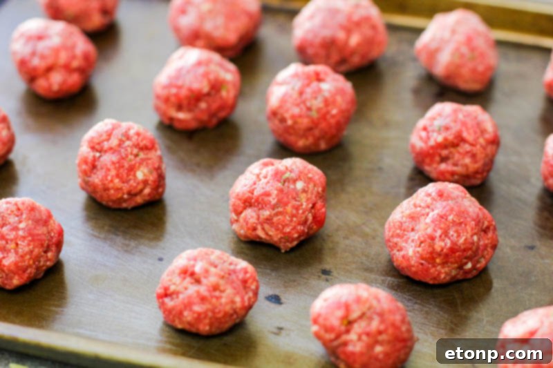 Freshly baked homemade meatballs, retaining their perfect spherical shape, arranged on a baking sheet.
