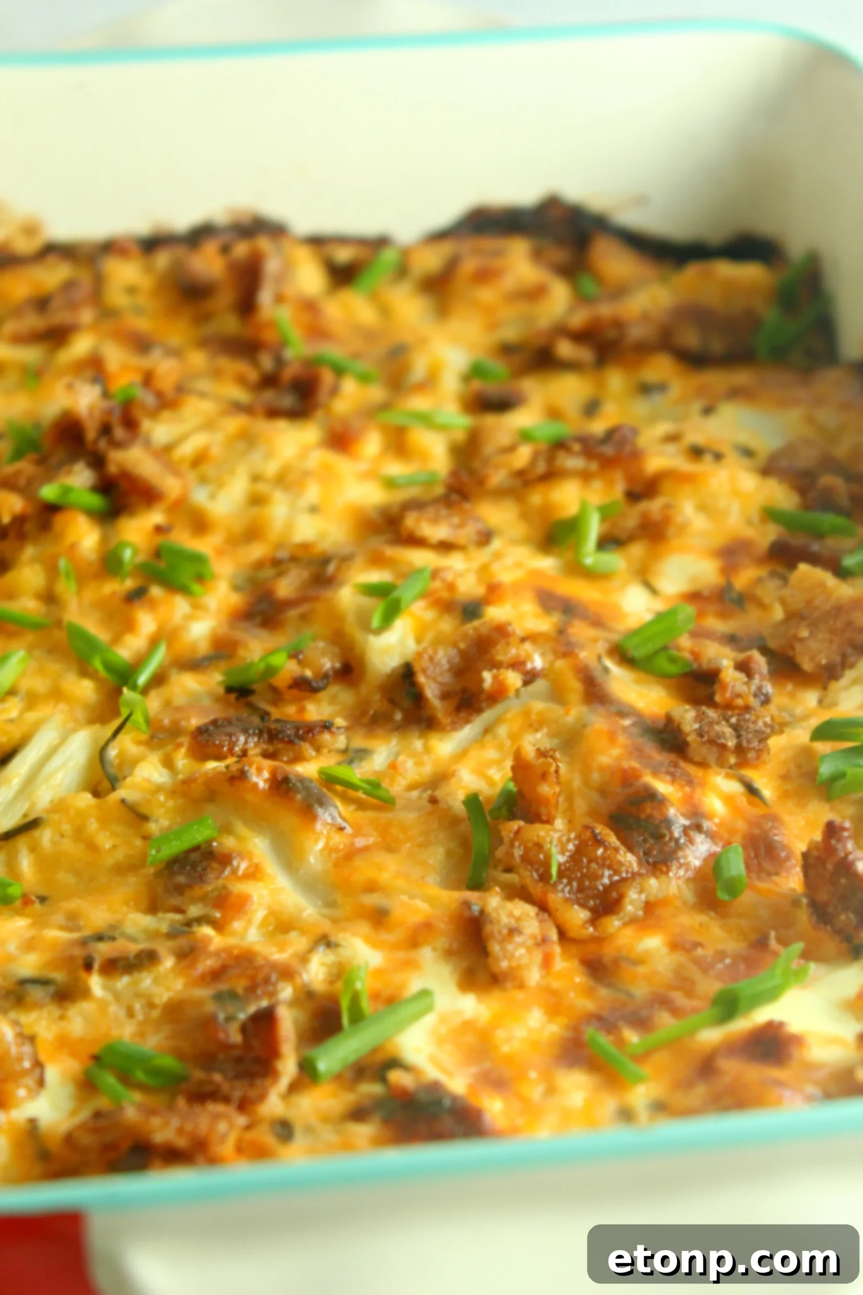 A serving of Loaded Cheesy Cauliflower Casserole on a plate, garnished with fresh green onions, ready to eat.