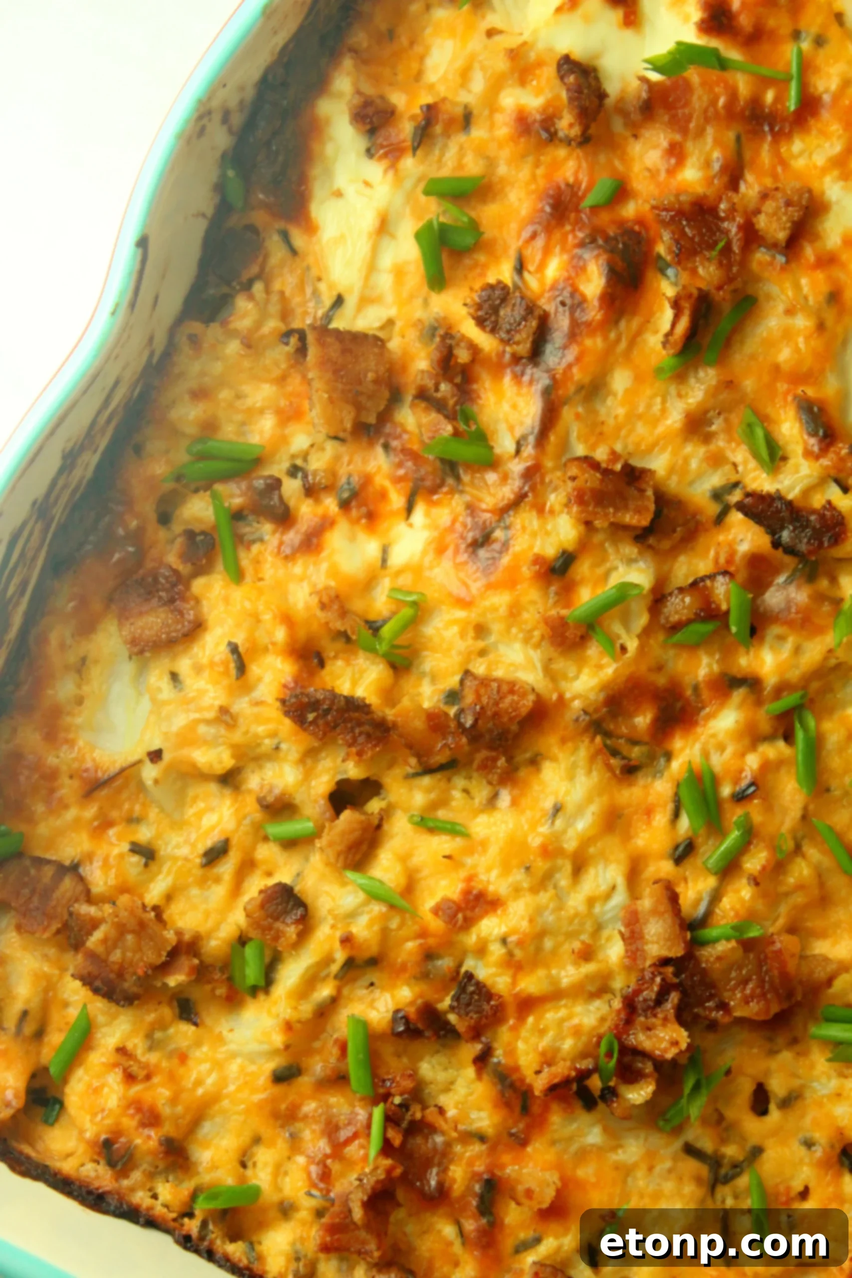 Another view of the Loaded Cheesy Cauliflower Casserole in a baking dish, with a serving spoon removing a portion.