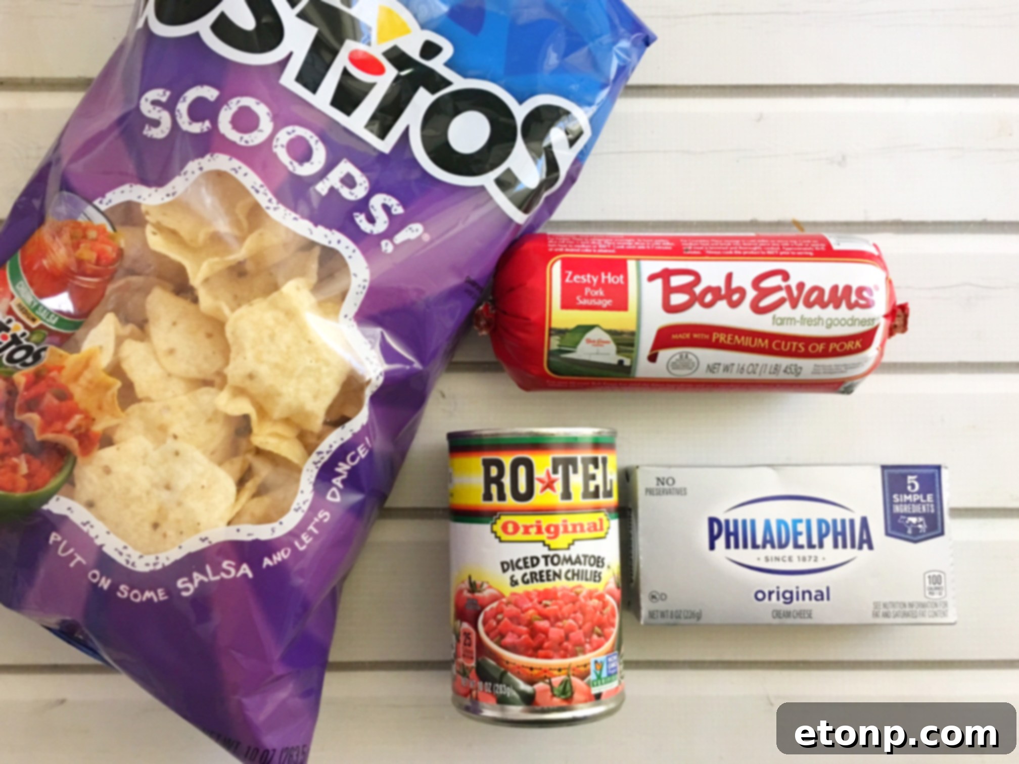 An overhead shot of a bubbly, hot spicy sausage dip in a skillet, with a serving spoon resting in it, surrounded by tortilla chips.