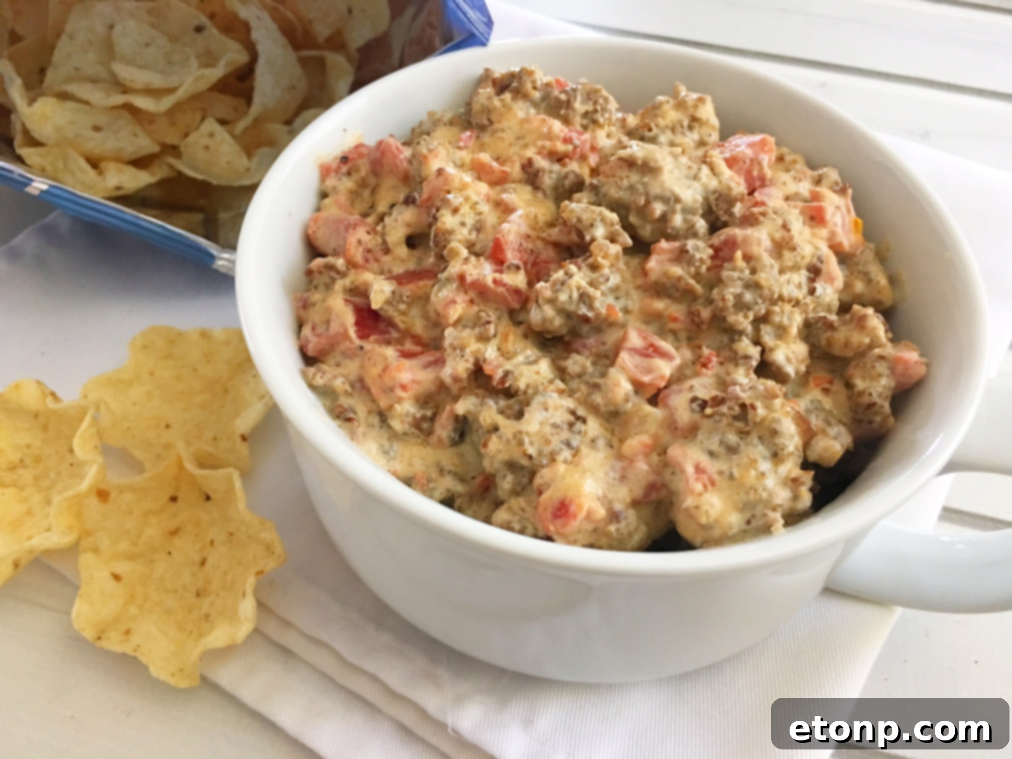A festive spread of Super Bowl snacks, featuring a large bowl of spicy sausage dip as the centerpiece, surrounded by various dippers and other appetizers.
