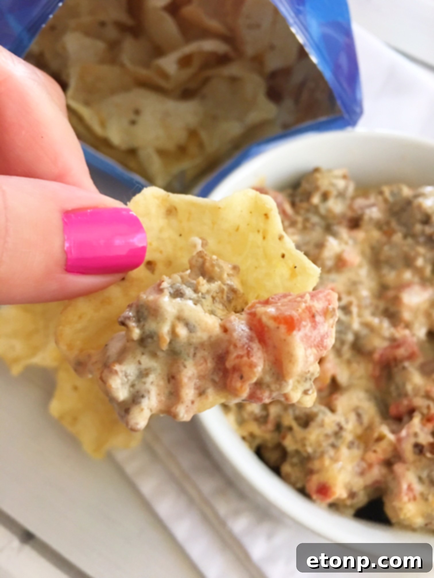 A vertical shot of the spicy sausage dip in a white bowl, with a few fresh tortilla chips placed around it, ready for dipping.