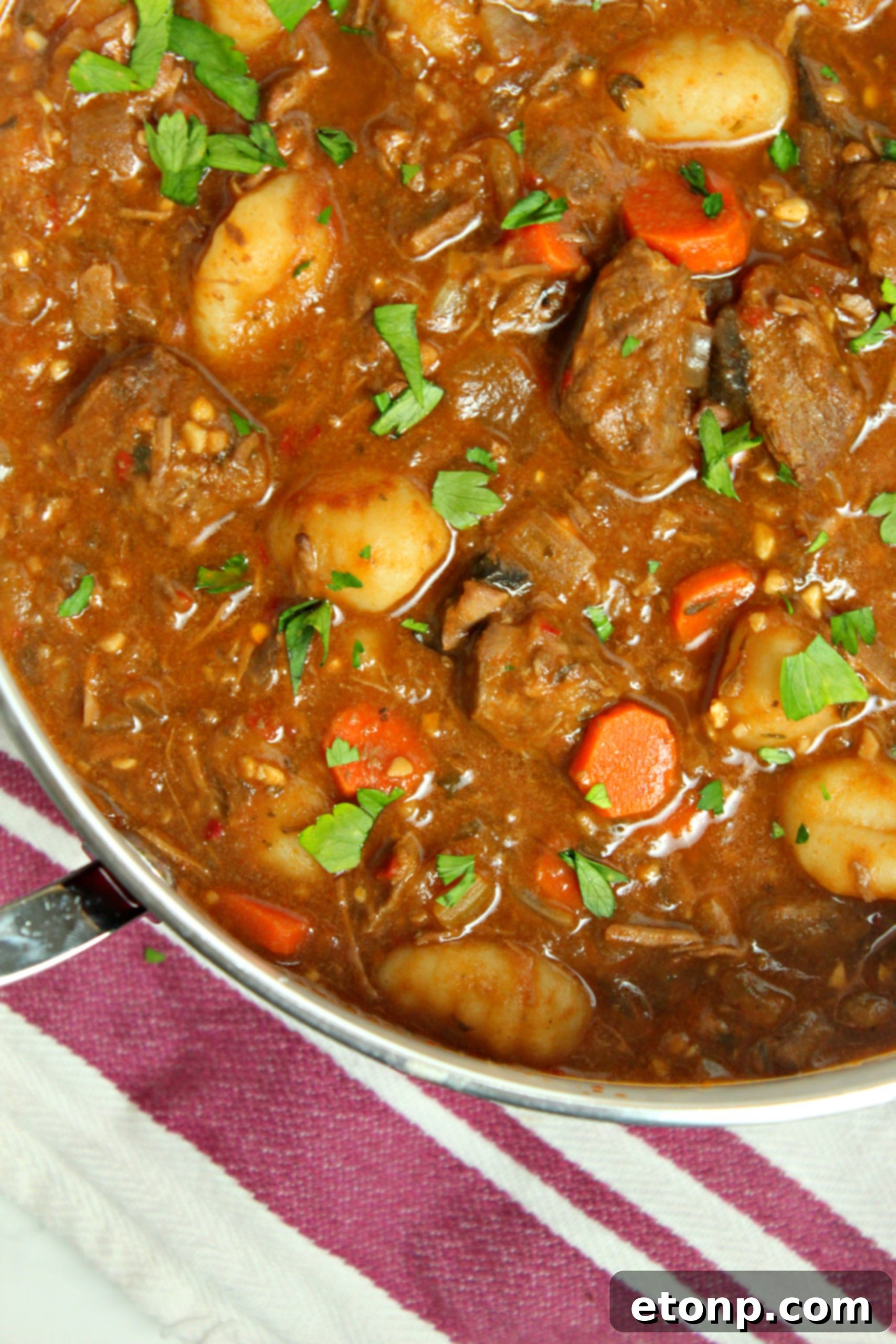 A spoonful of chunky beef and gnocchi soup being lifted from the pot, showing the thick, rich broth and hearty ingredients.