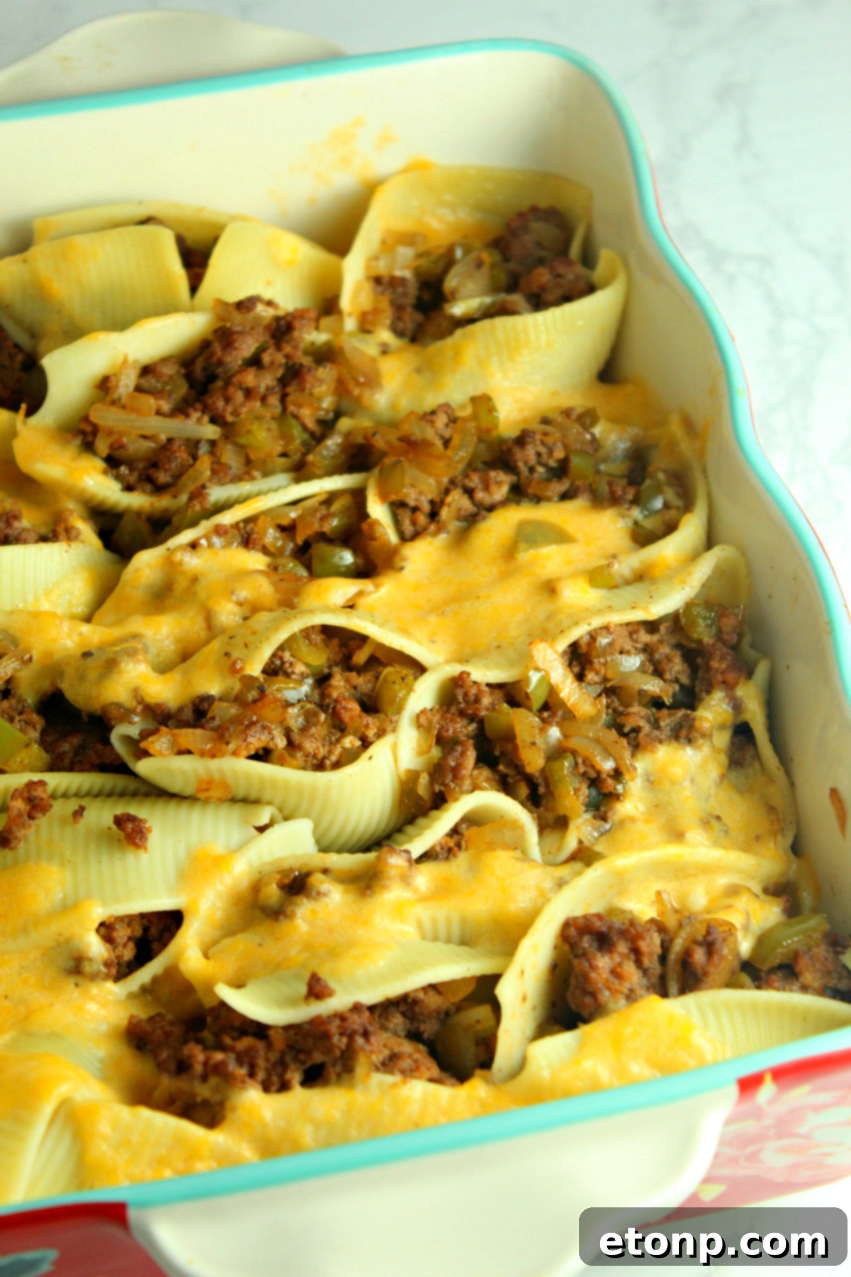 A dish of Philly Cheese Steak Stuffed Shells with a creamy cheese sauce pooling around them.