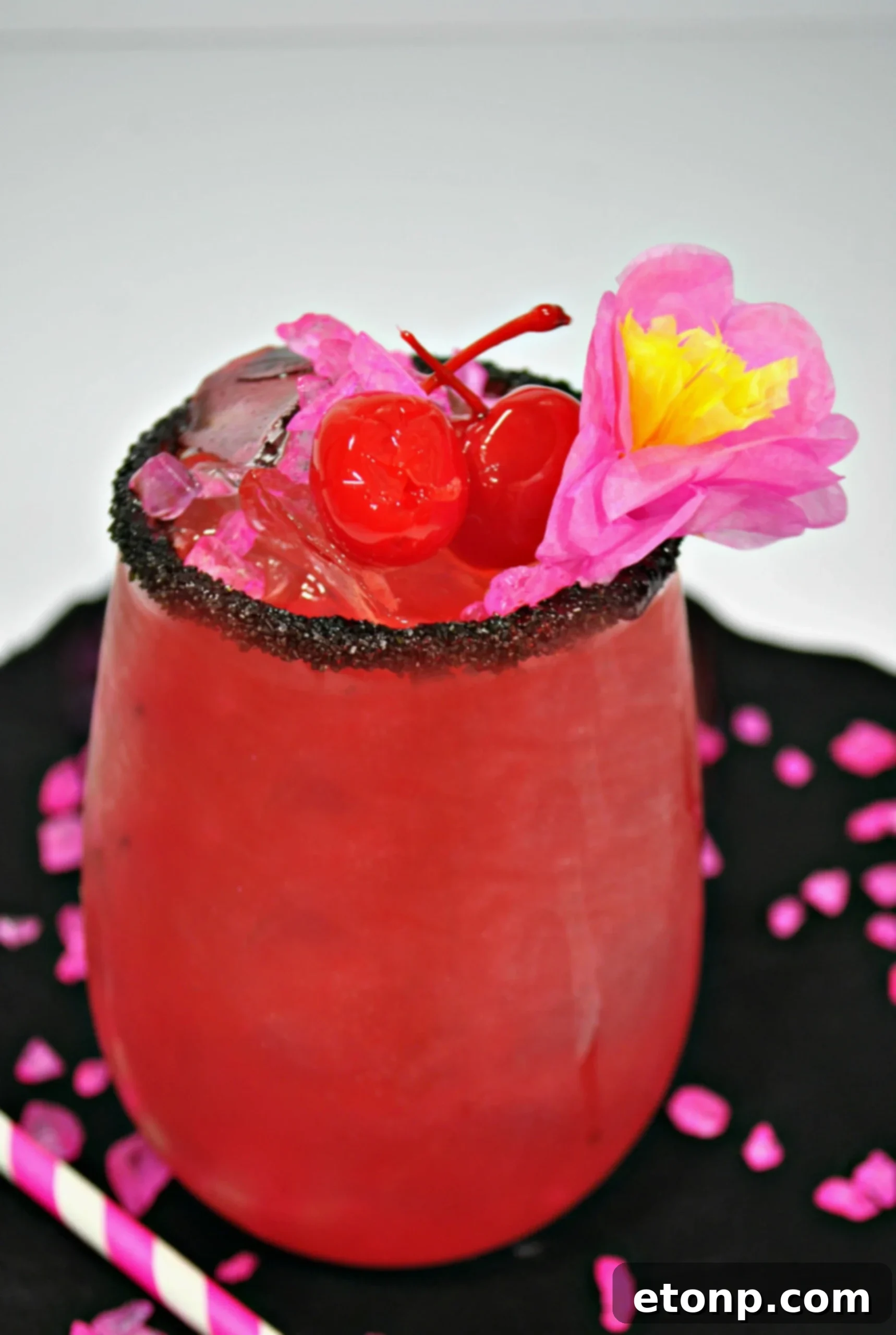 A vibrant pink Barbie cocktail adorned with a lime wedge and cherries, in a glass rimmed with black sprinkles, ready for a fun girls' night.